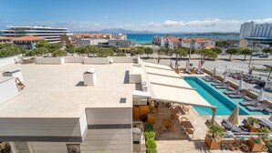 A rooftop pool area with lounge chairs, umbrellas, and a view of the sea. - Twins Hotel (Cesme)
