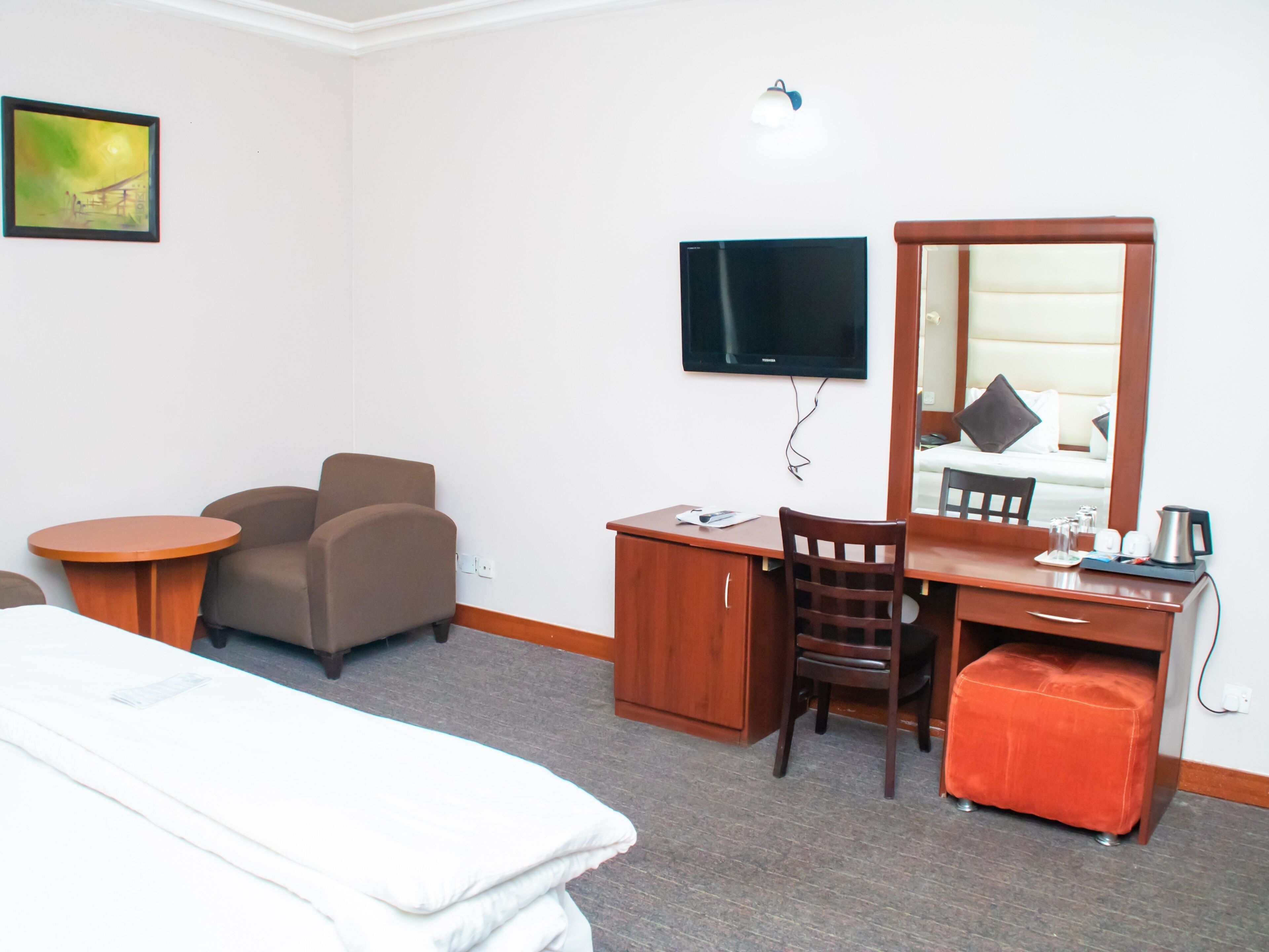 Een hotelkamer met een bed, een bureau, een stoel, een kleine tafel, een televisie en een schilderij aan de muur.