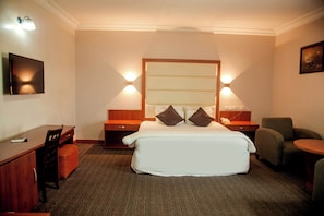 A hotel room with a bed, bedside tables, a desk, a chair, and a television. - Denis Hotel (Abuja)