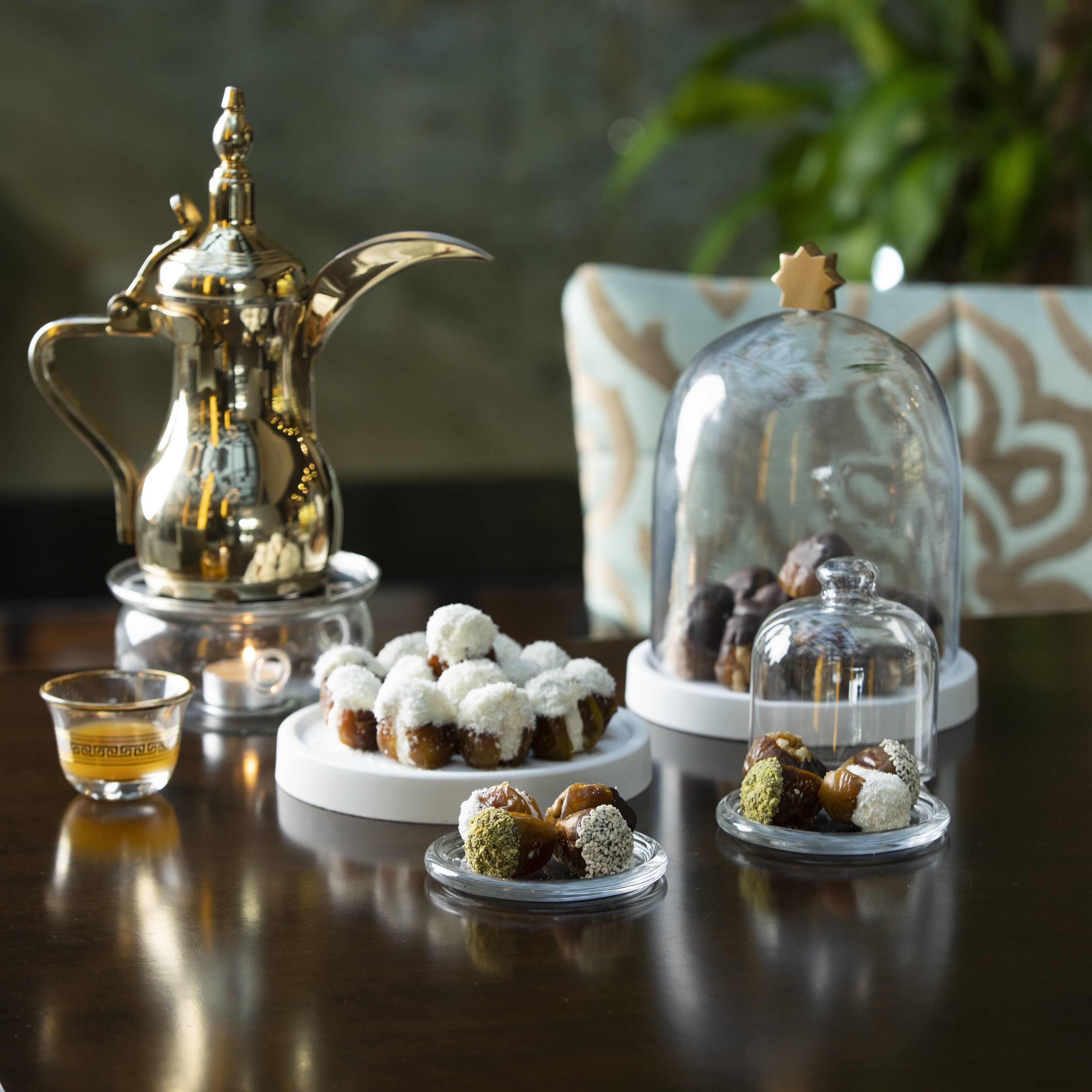 Una mesa con un juego de té de plata, una campana de cristal con pasteles, y una taza pequeña de té.