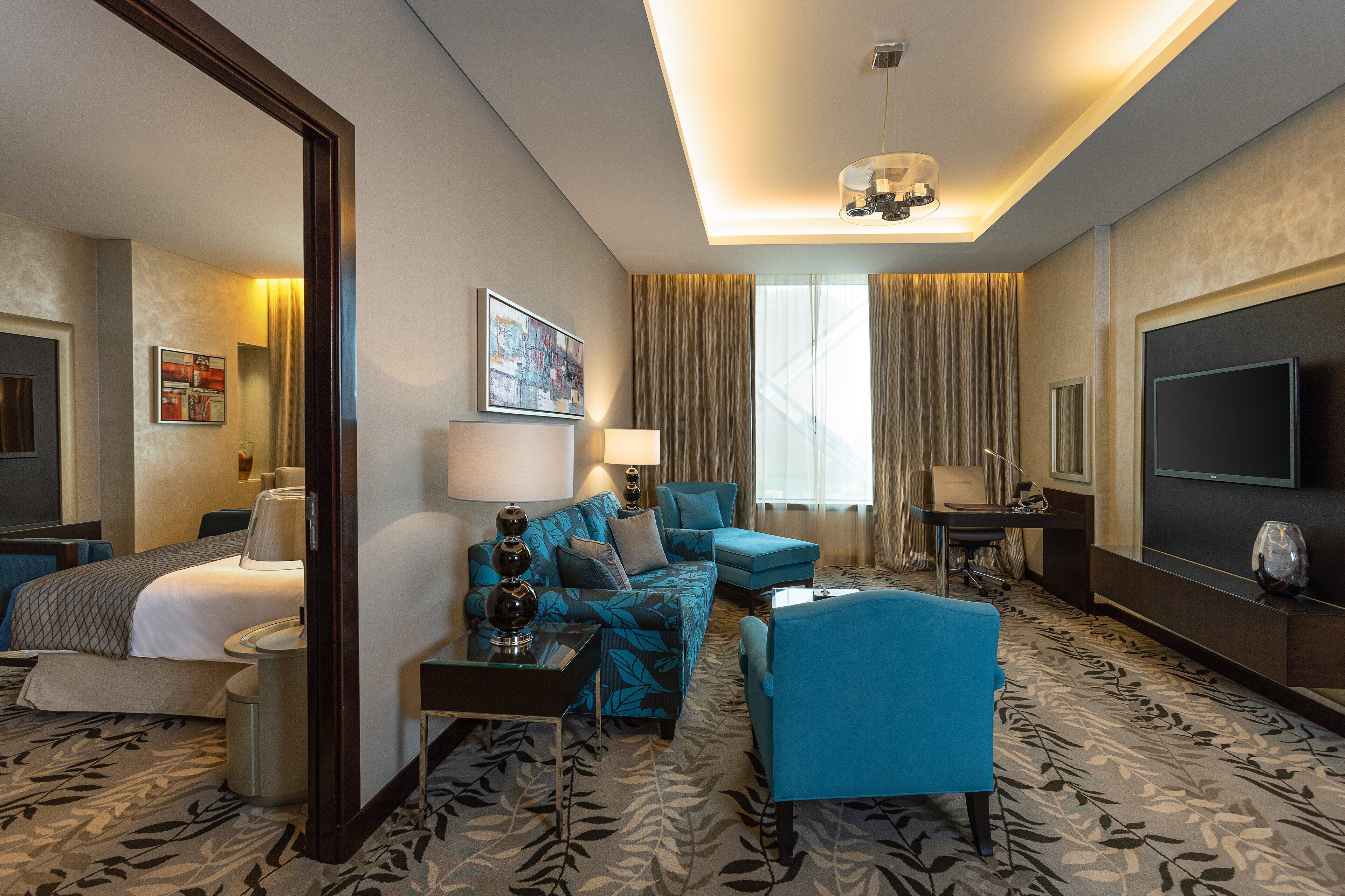 A hotel room with a bed, a sofa, a chair, a desk, a TV, and a large window with curtains.