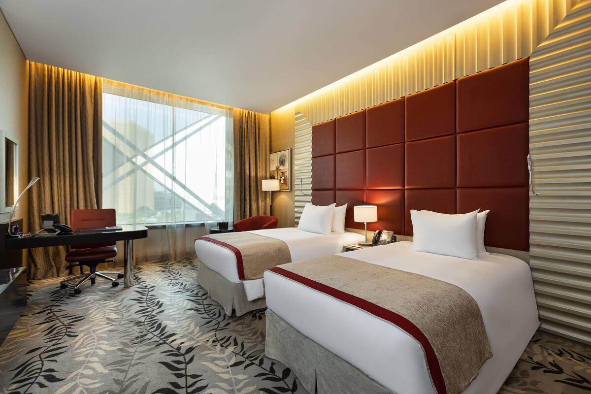 A hotel room with two beds, a desk, a chair, and a large window with curtains.