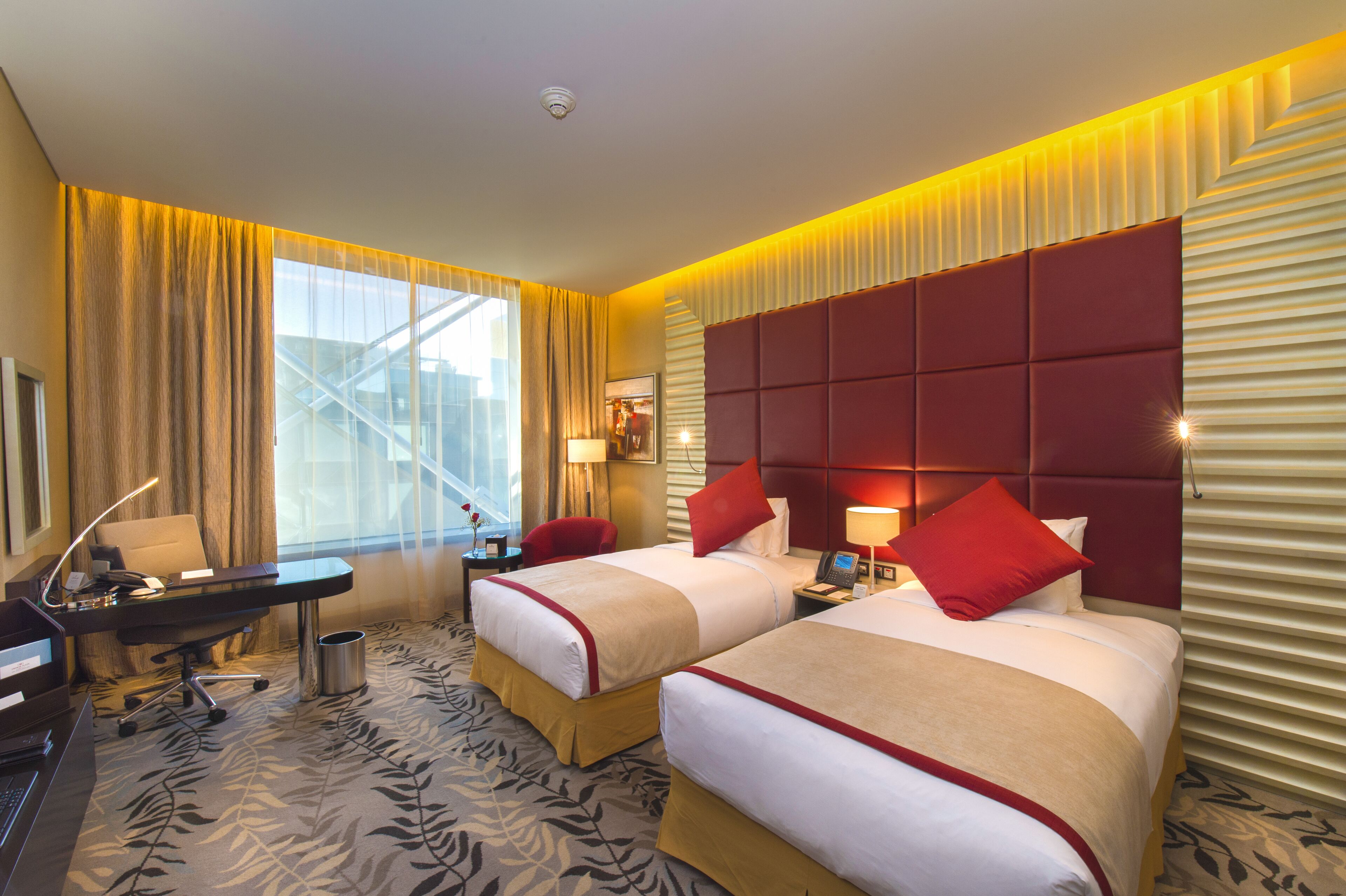 A hotel room with two beds, a desk, a chair, a lamp, and a window with curtains.