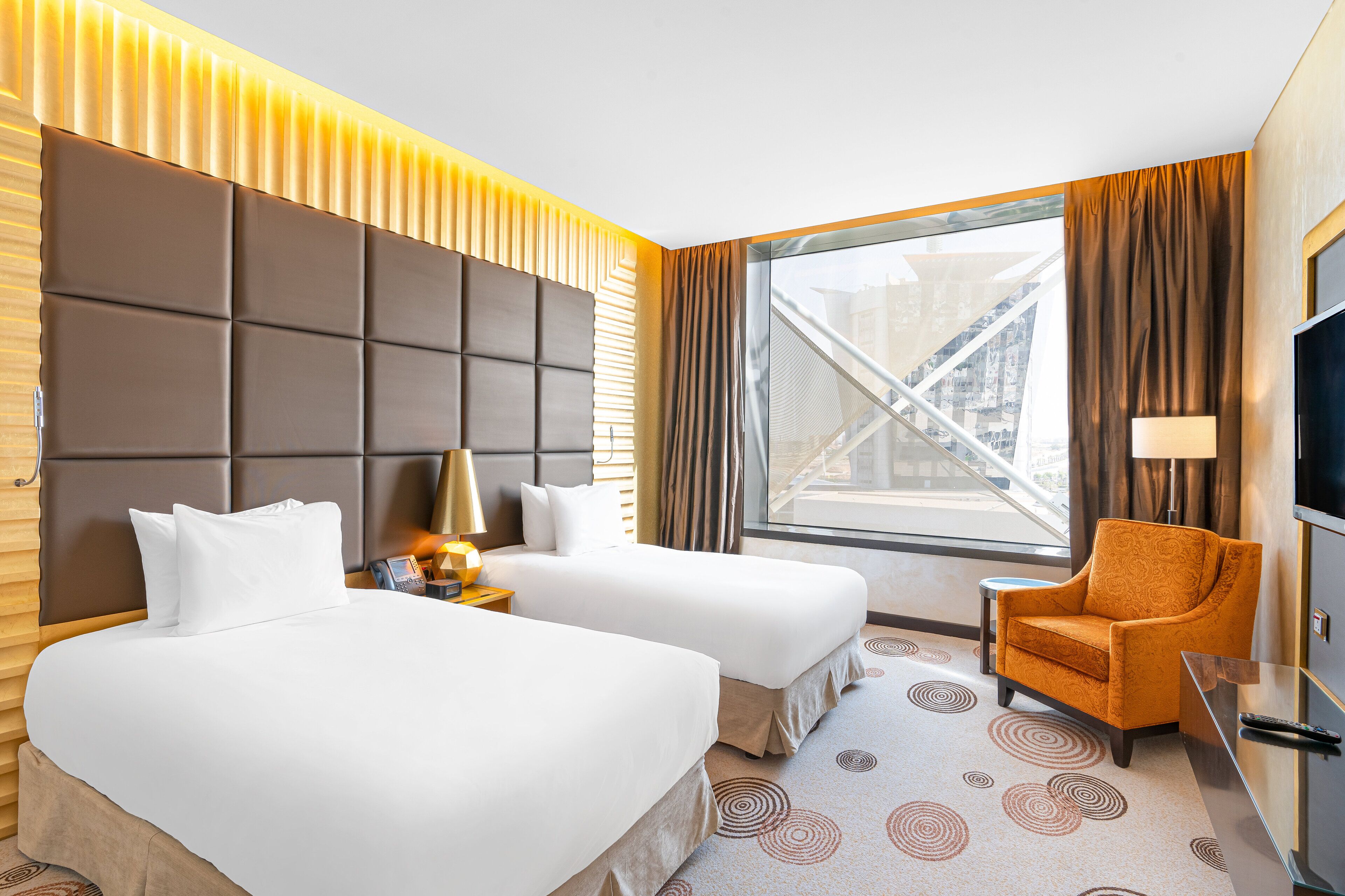 A hotel room with two beds, a sofa, a TV, and a window with a city view.