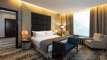 Ein Hotelzimmer mit einem großen Bett, einem Schreibtisch, einem Sessel und Blick auf ein Gebäude durch das Fenster.