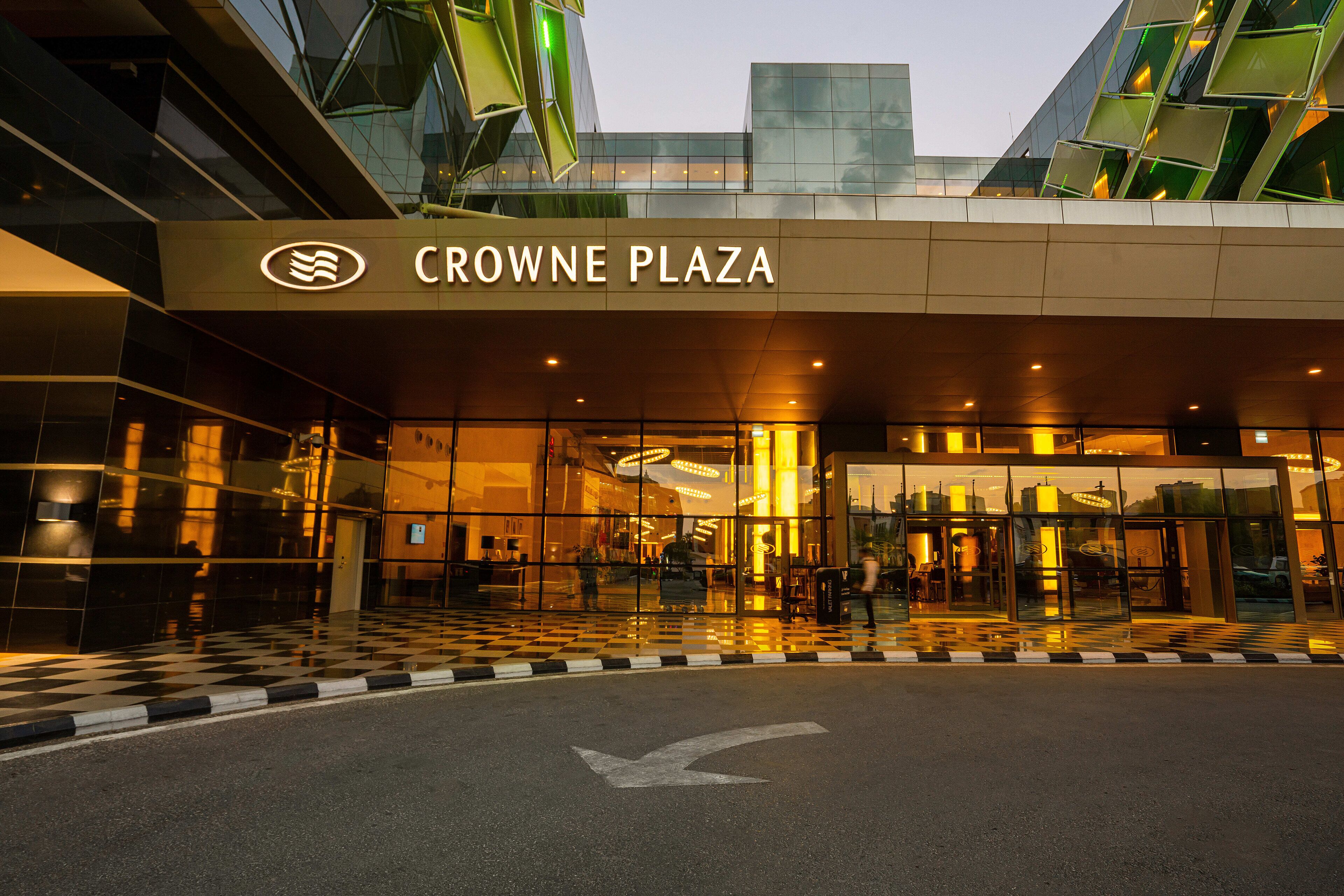 The exterior of Crowne Plaza with a checkered floor pattern, a prominent entrance, and a glass facade reflecting the surroundings.