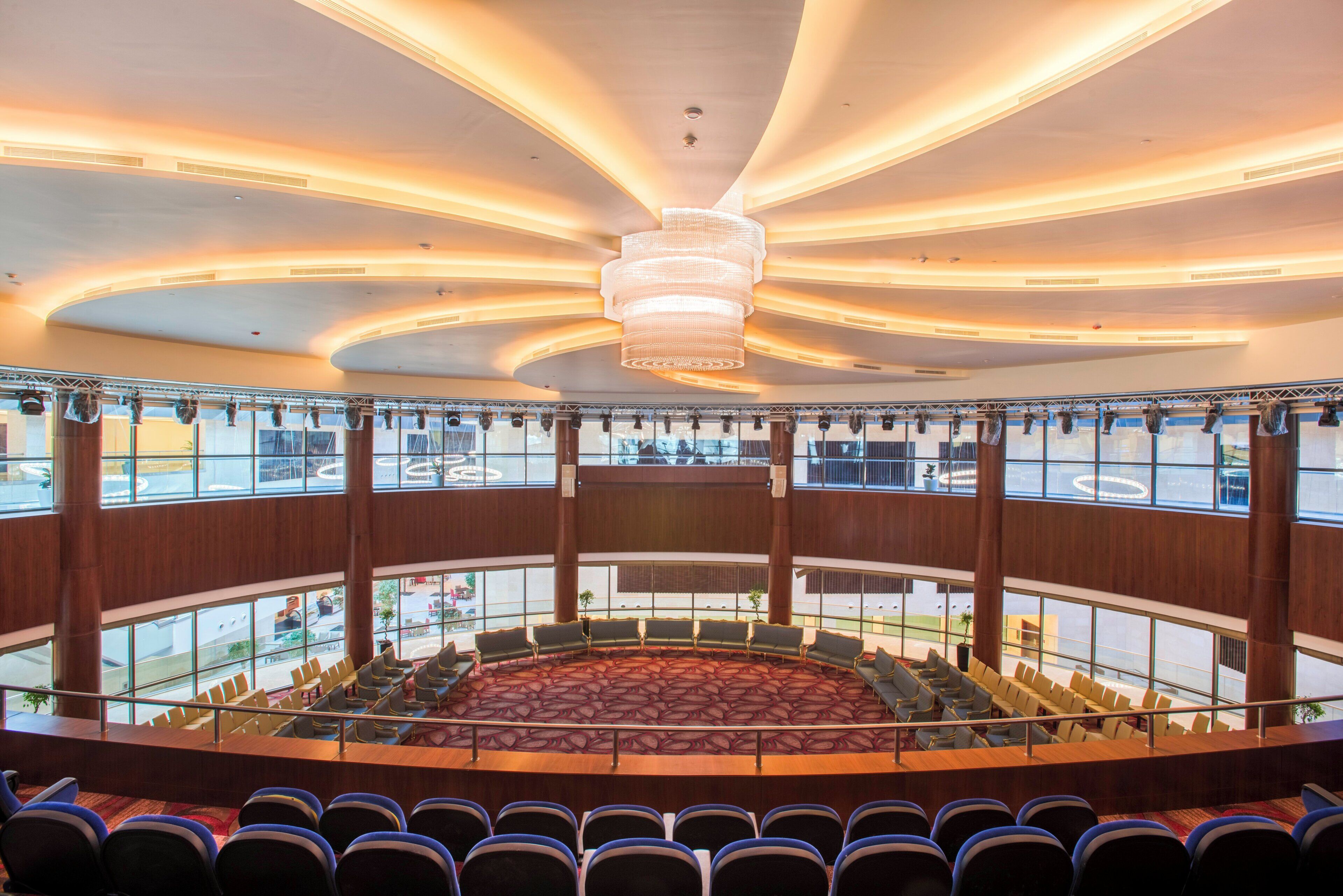 A conference room with tiered seating, a large chandelier, and multiple windows offering views of the outside.