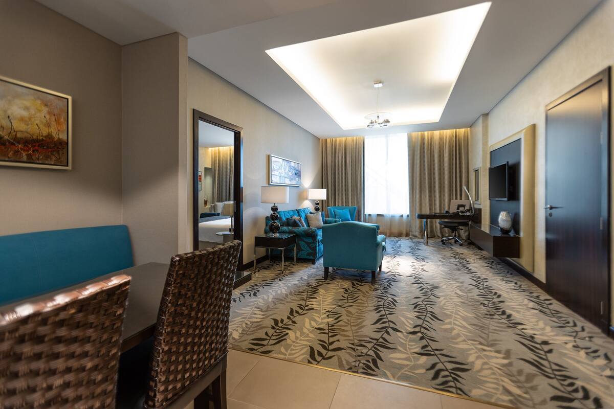 A hotel room with a large bed, a sitting area with a sofa and chairs, a desk with a computer, and a television.