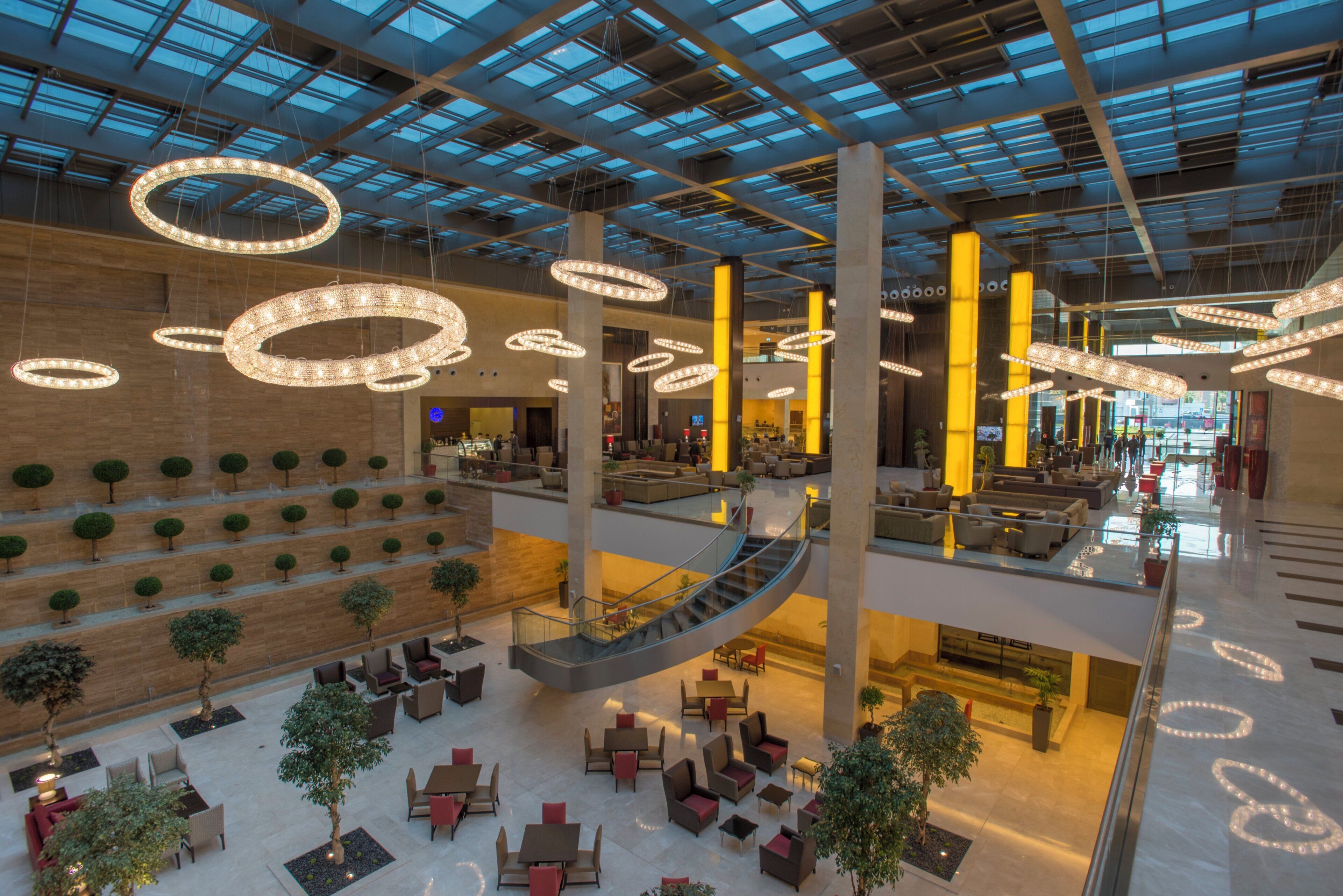 A spacious atrium with multiple levels, featuring a central staircase, seating areas, and hanging circular light fixtures.