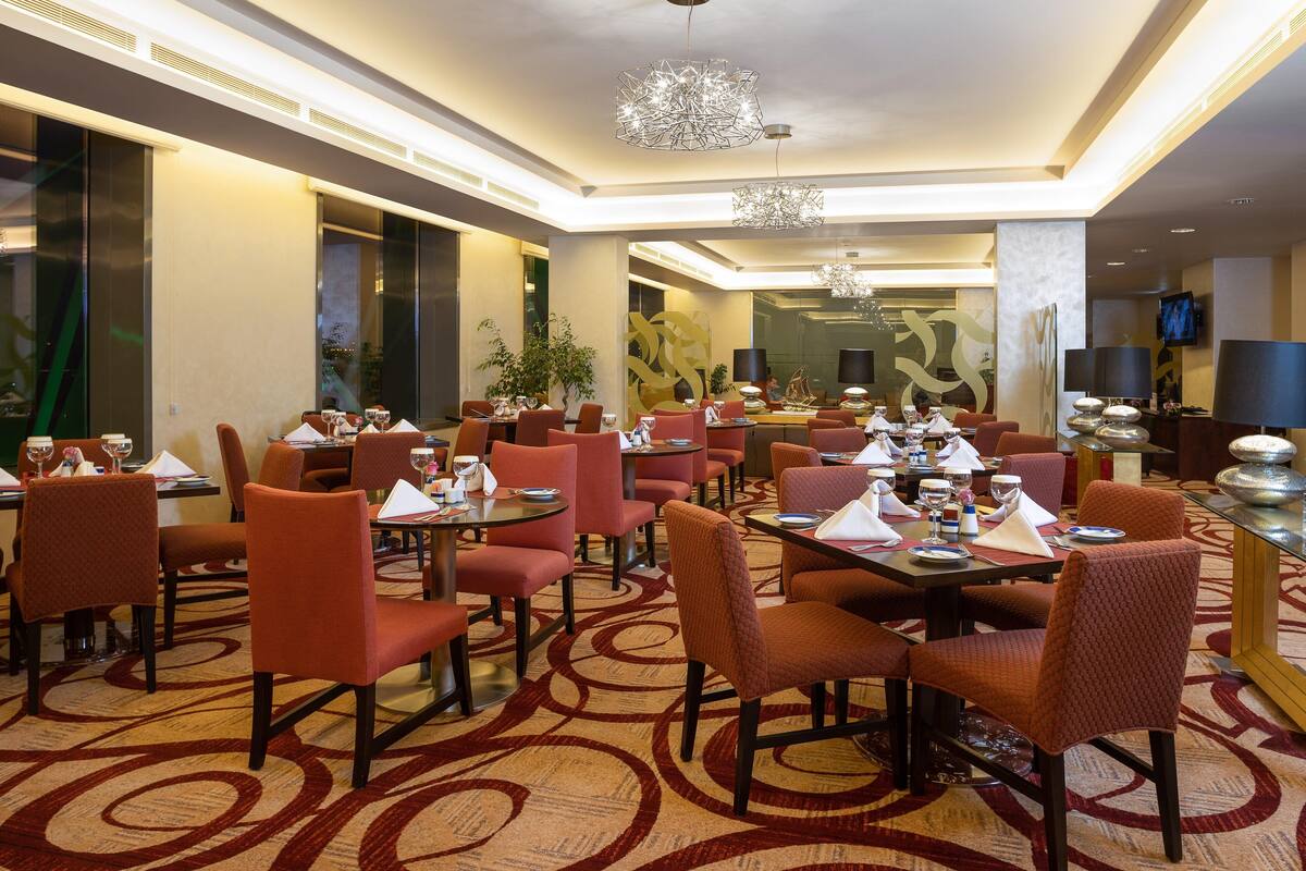 A hotel dining area with multiple tables and chairs, large windows, and modern decor.