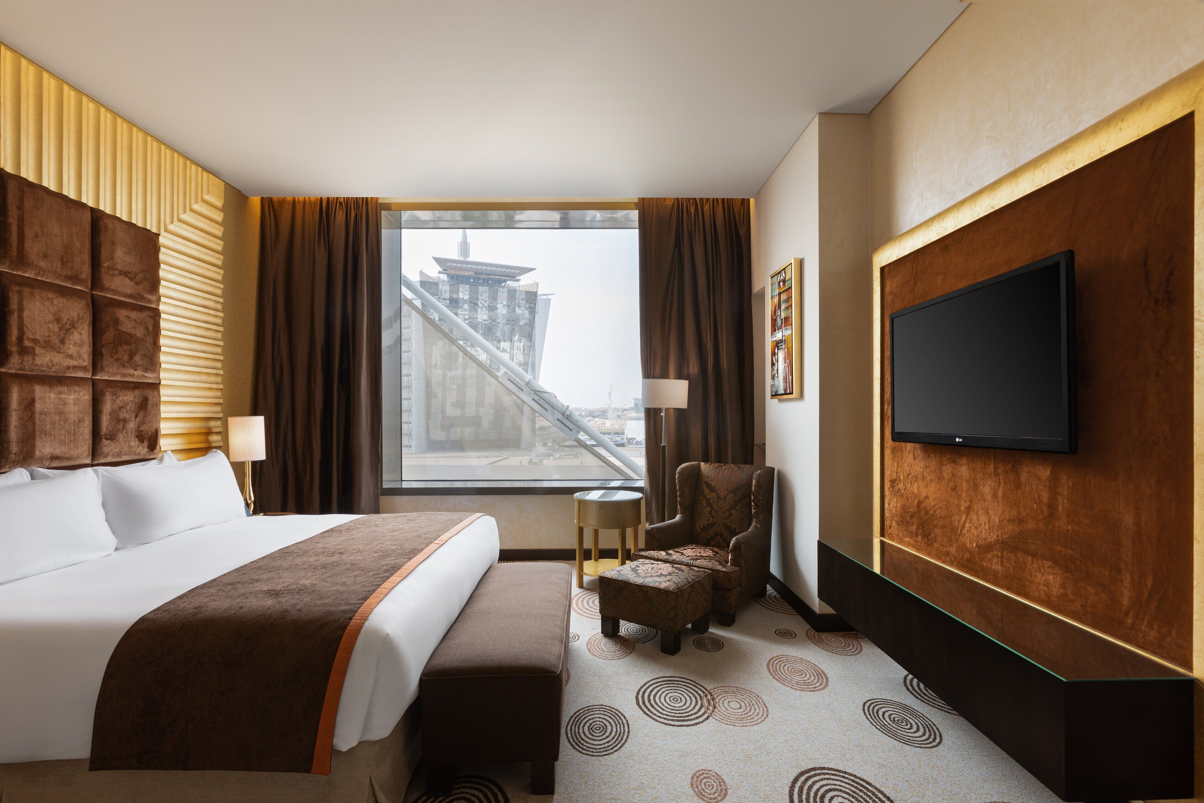 A hotel room with a large bed, a chair, a TV, and a window with a view of a building.