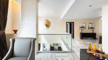 A modern hotel lobby with a marble floor, a grey armchair, a glass railing, and a breakfast tray with fruits and beverages.