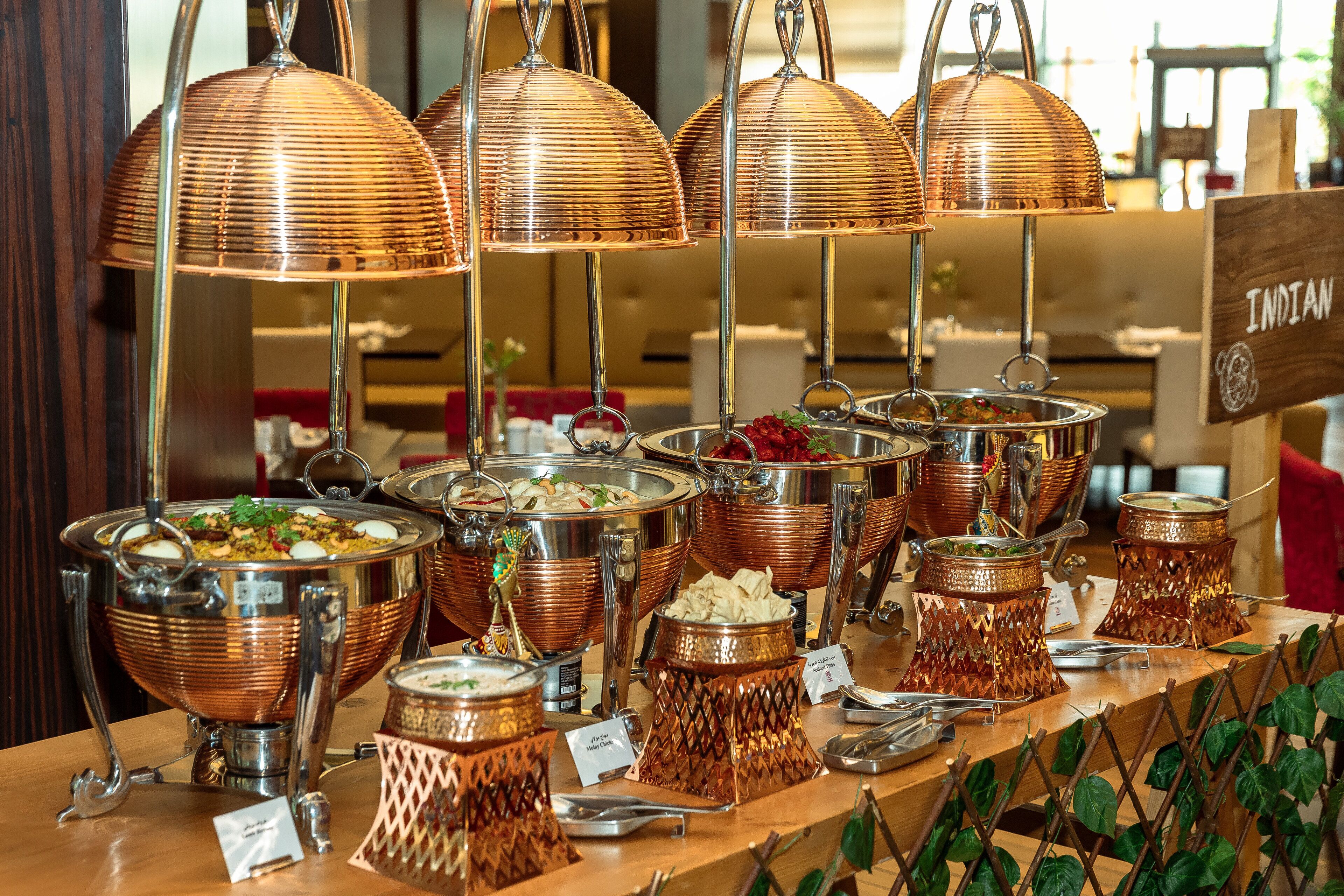 Un buffet avec de nombreux plats de service en cuivre et un panneau indiquant qu’il propose de la « cuisine indienne ».