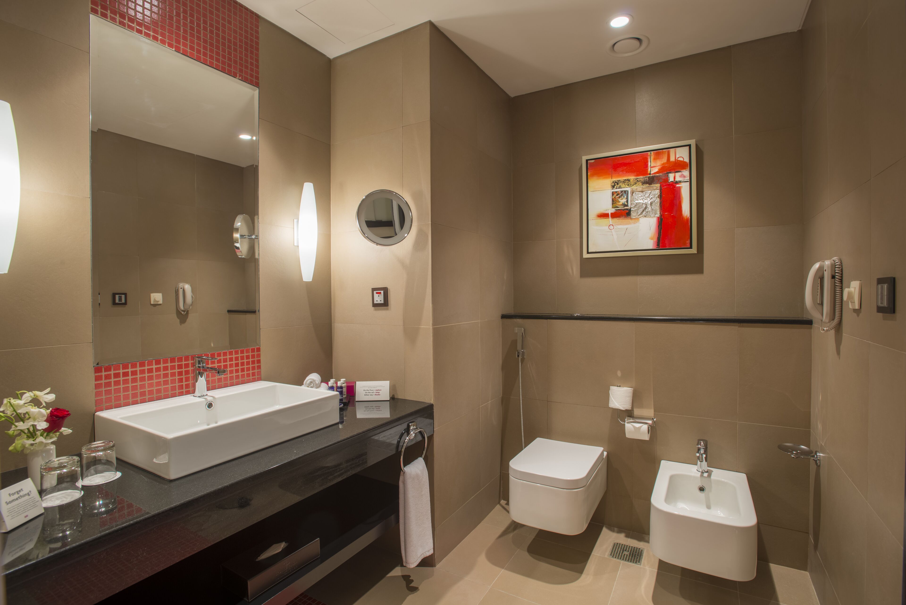 Une salle de bain moderne avec un grand lavabo, des toilettes et un bidet. On y trouve un miroir, un porte-serviettes et un tableau encadré au mur.