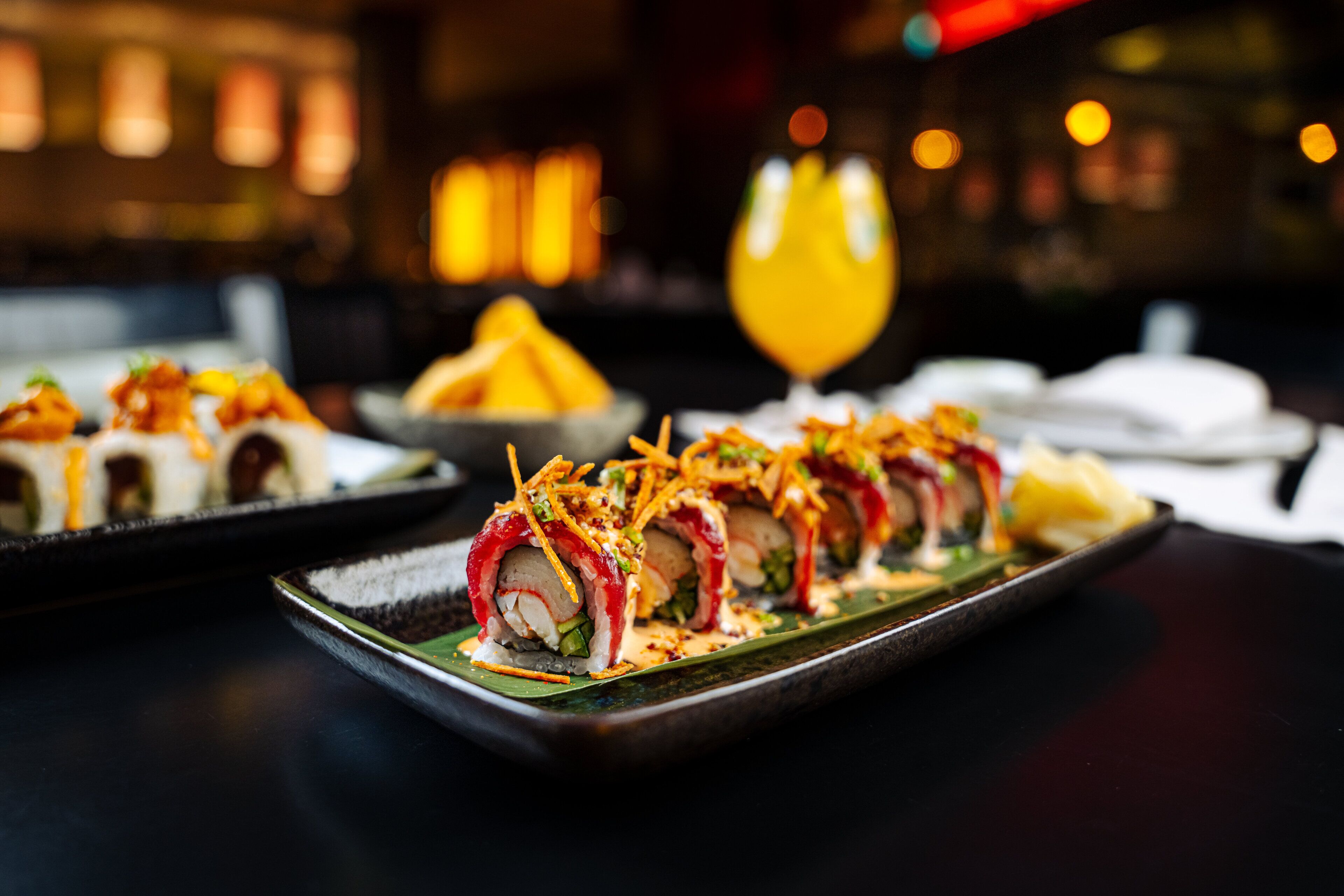 Sushi dishes on a black plate with a green leaf underneath.
