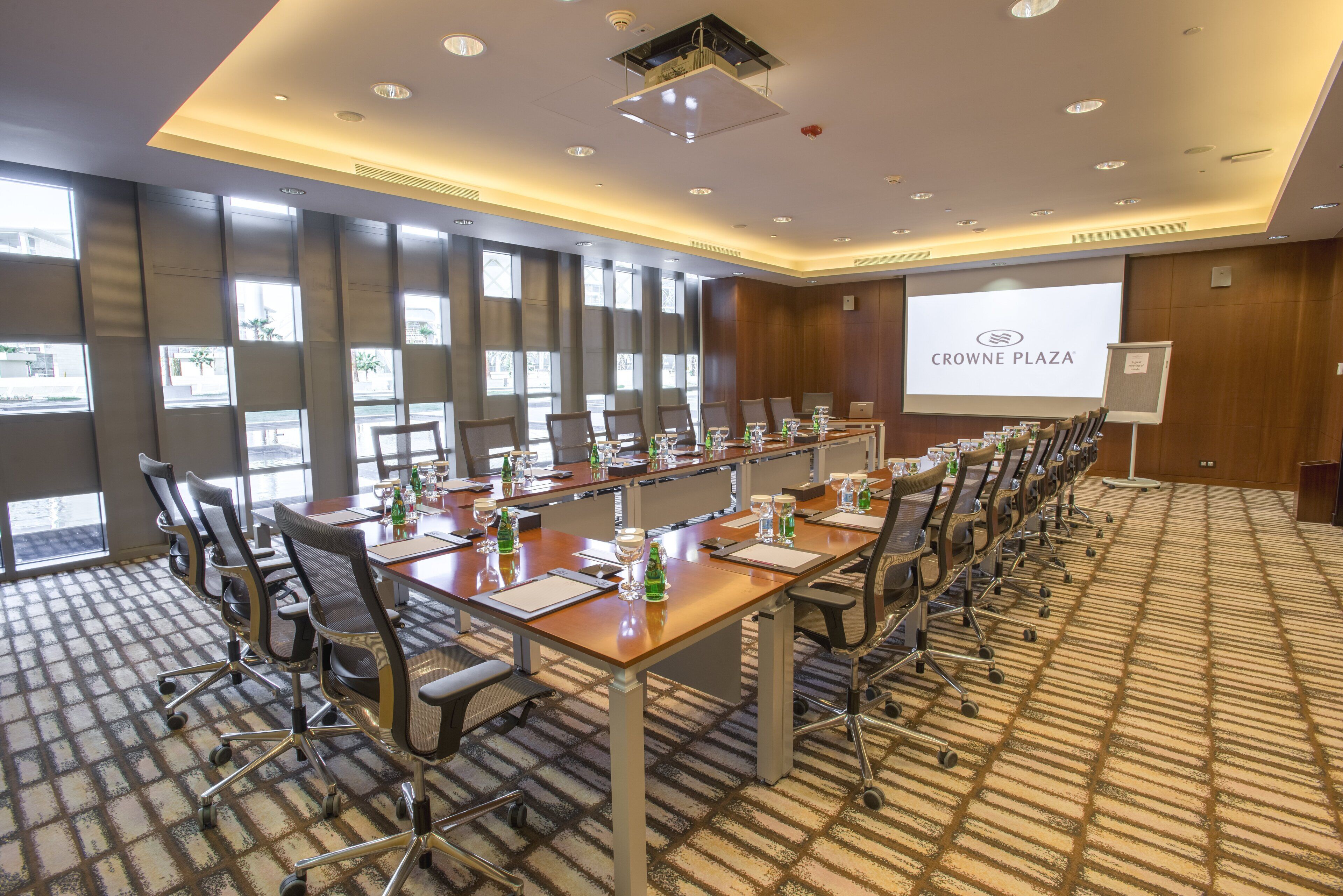 A conference room with a long table, chairs, and a projector screen displaying "CROWNE PLAZA".