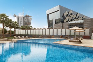 A swimming pool with lounge chairs and umbrellas, surrounded by palm trees and modern buildings. - Crowne Plaza Riyadh RDC Hotel & Convention by IHG (Riyadh)