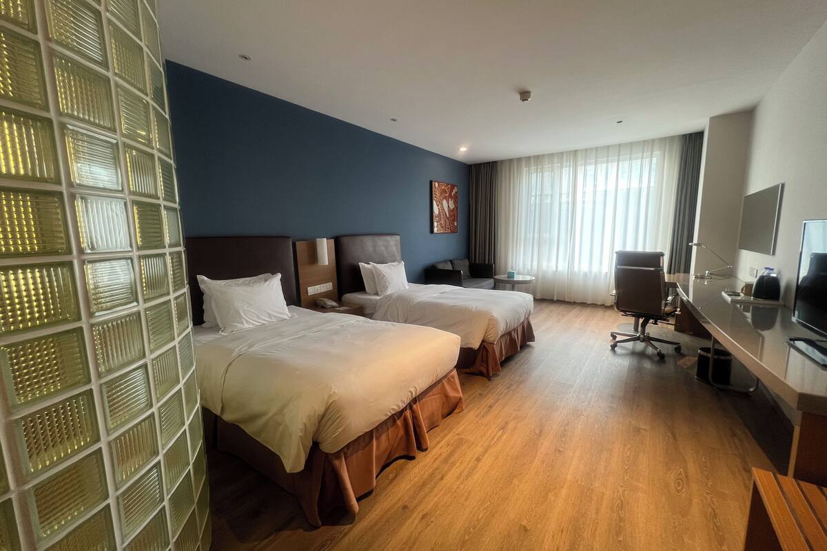 A hotel room with two beds, a desk, a chair, a TV, and a window with curtains.