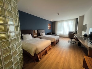 Une chambre d’hôtel avec deux lits, un bureau, une chaise, une télévision et une fenêtre avec des rideaux.