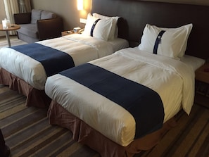 Une chambre d’hôtel avec deux lits, chacun agrémenté de draps blancs et bleus, une petite table avec une lampe et une chaise.