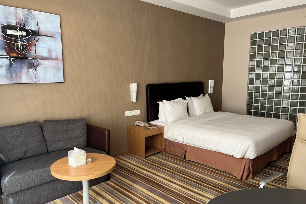 A hotel room with a large bed, a sofa, a small table, and a wall-mounted TV.