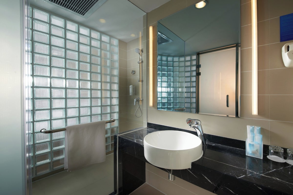 Une salle de bain avec une douche à parois de verre, un lavabo blanc et un miroir qui reflète la douche.
