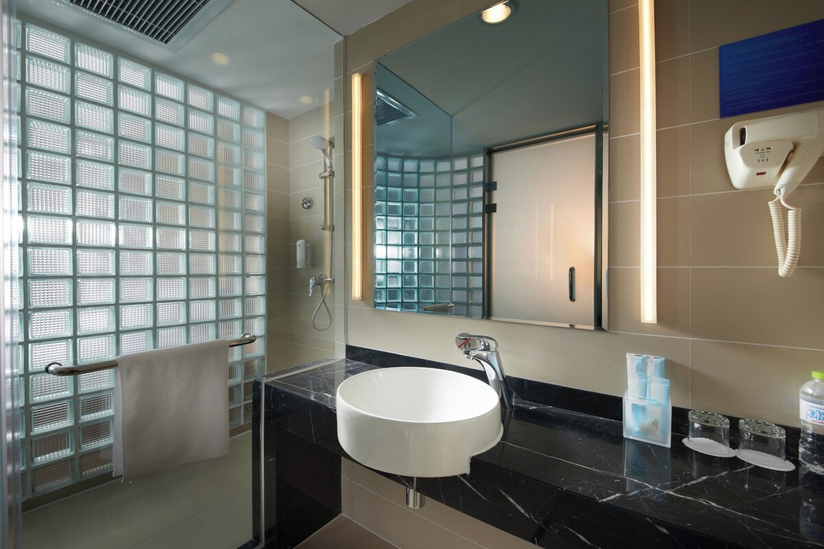 A bathroom with a glass shower enclosure, a white sink, and a mirror.