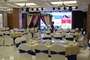 A banquet hall with round tables set for a formal event, featuring white chairs with blue sashes, and a stage with a floral backdrop. - Holiday Inn Express Ordos Dongshen by IHG (Ordos)