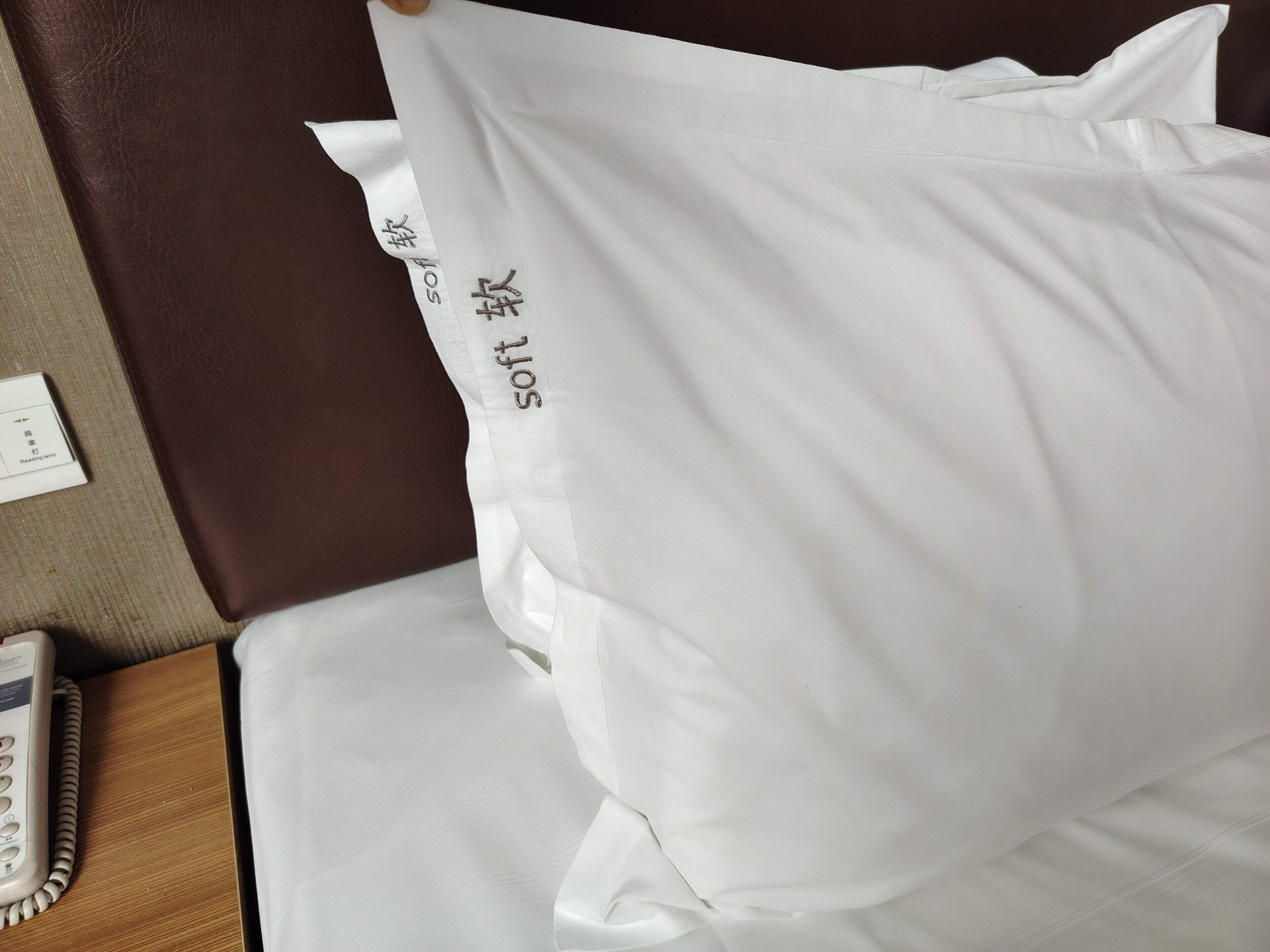 A white pillow with embroidered text on a bed.