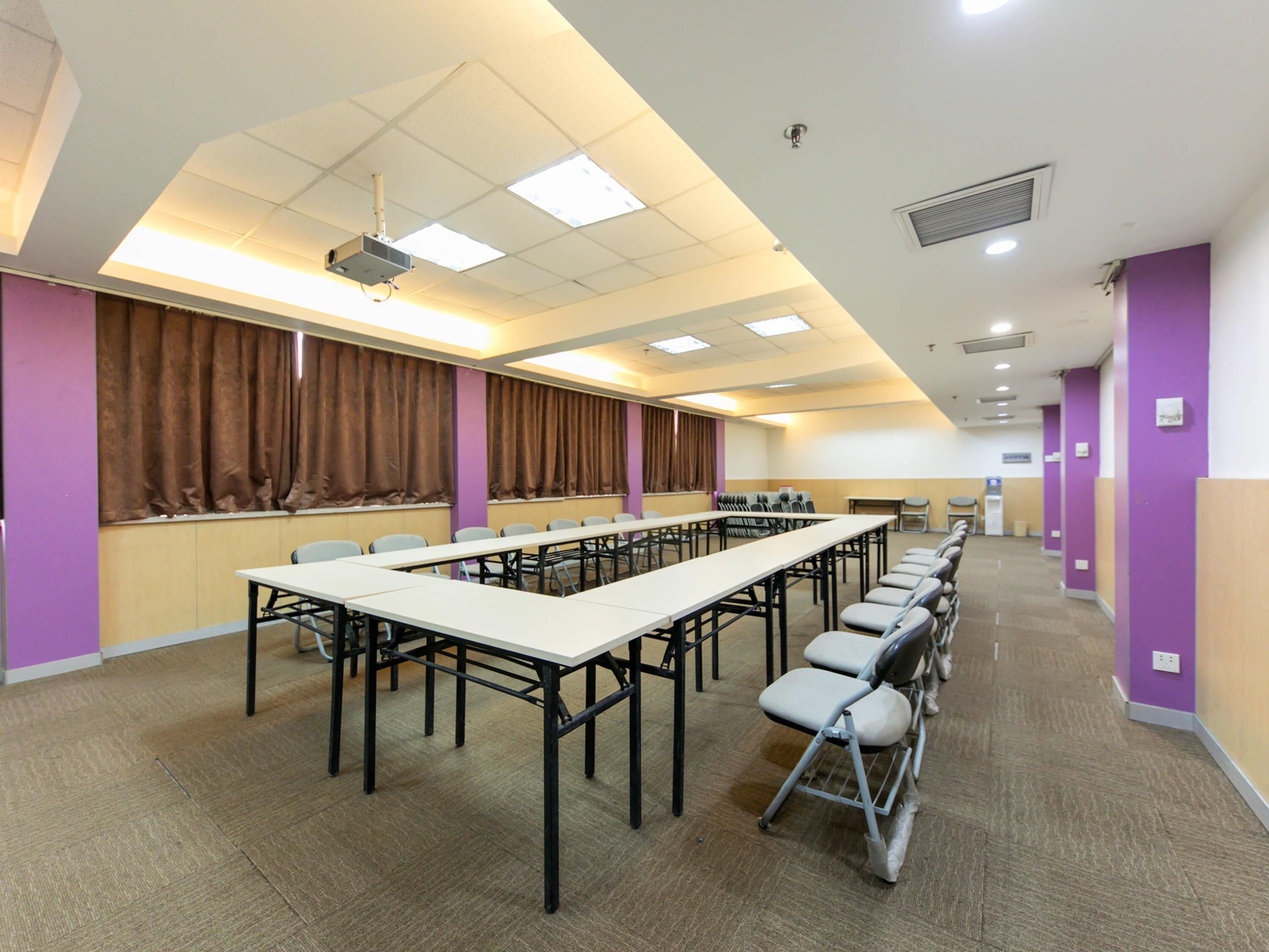 Une salle de conférence équipée de longues tables, de chaises, d’un projecteur et d’une estrade.