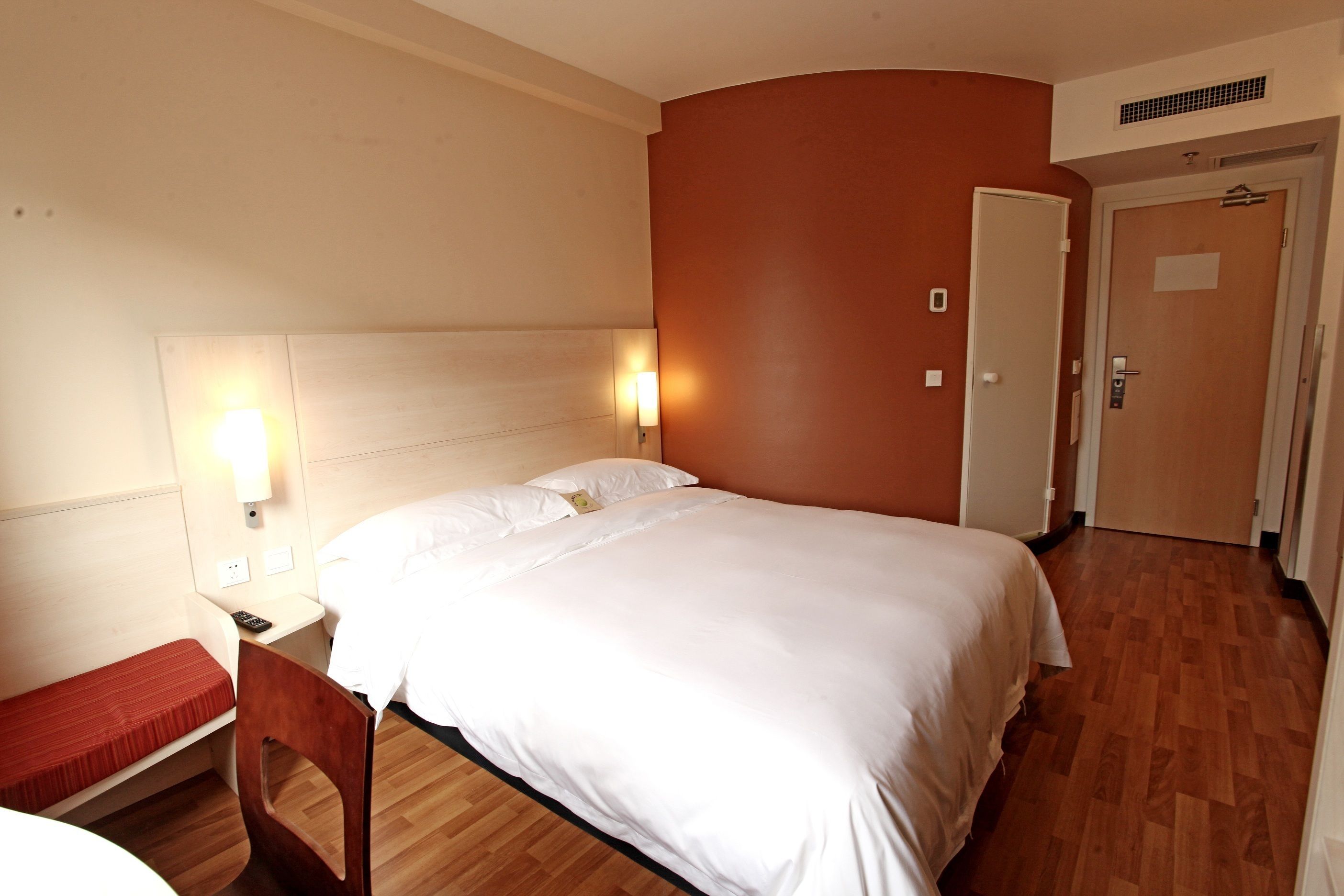 A hotel room with a bed, bedside table, chair, and a door.