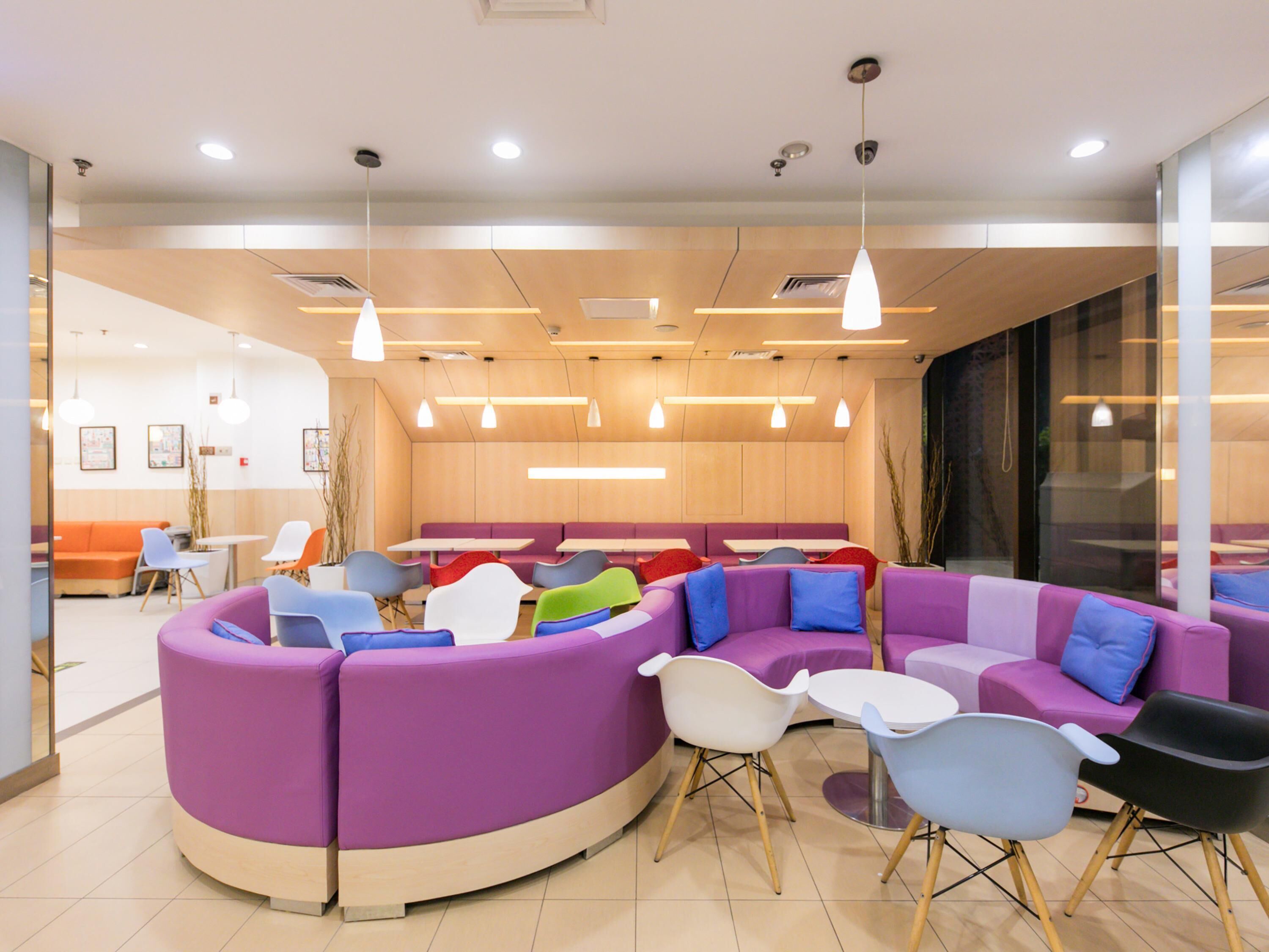 A modern interior with purple and white seating, wooden tables, and pendant lighting.