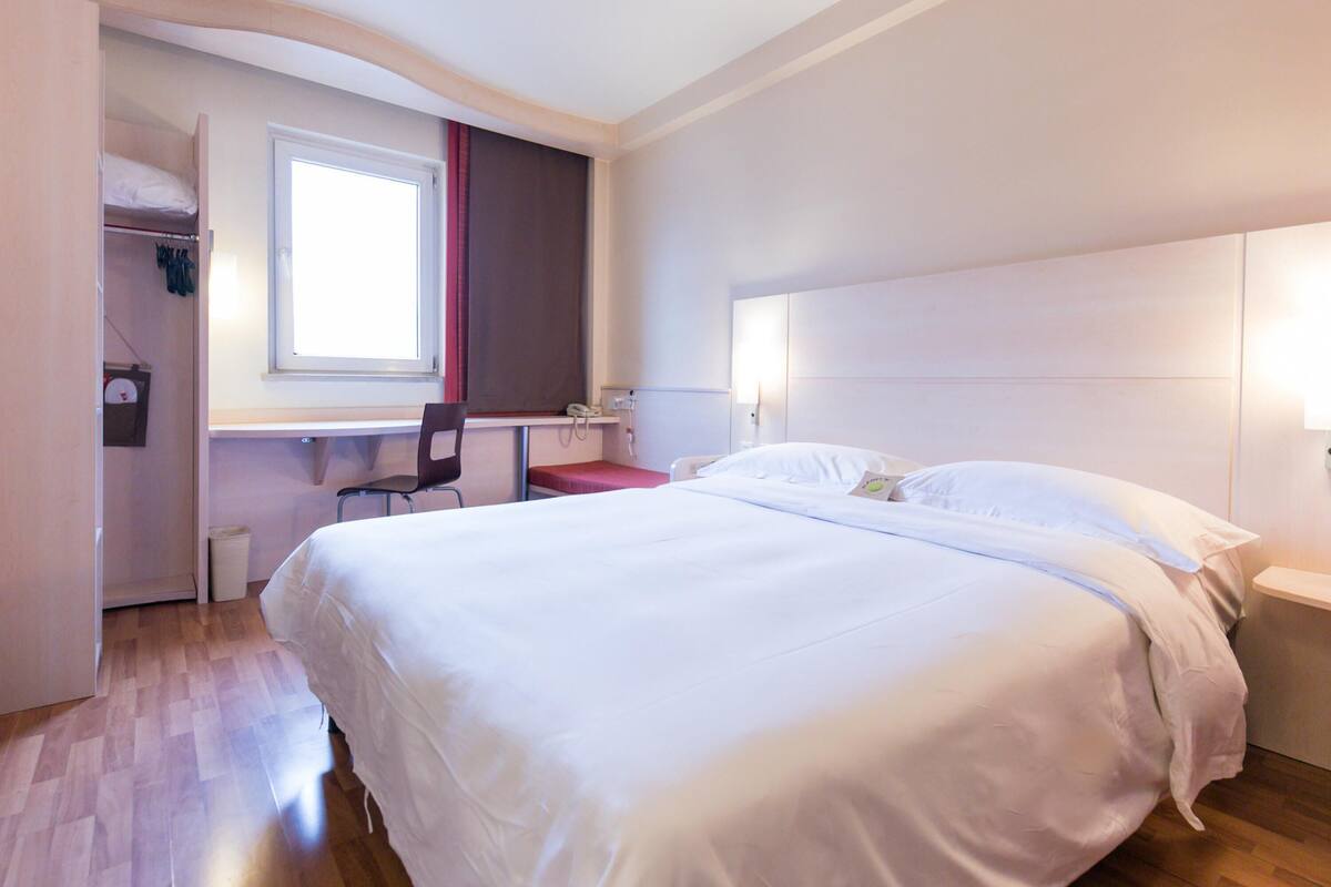 Una habitación de hotel con cama, escritorio, silla y ventana.