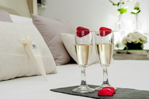 Due flute da champagne con fragole sul bordo, posate su un sottobicchiere di ardesia nera, con un cuscino bianco e un nastro decorativo sullo sfondo.