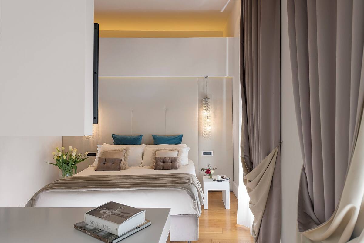 A modern bedroom with a large bed, bedside tables, a nightstand, and a hanging light fixture.