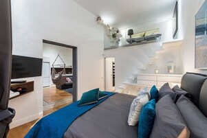Una camera da letto moderna con un letto, una sedia sospesa, una scala e un televisore.