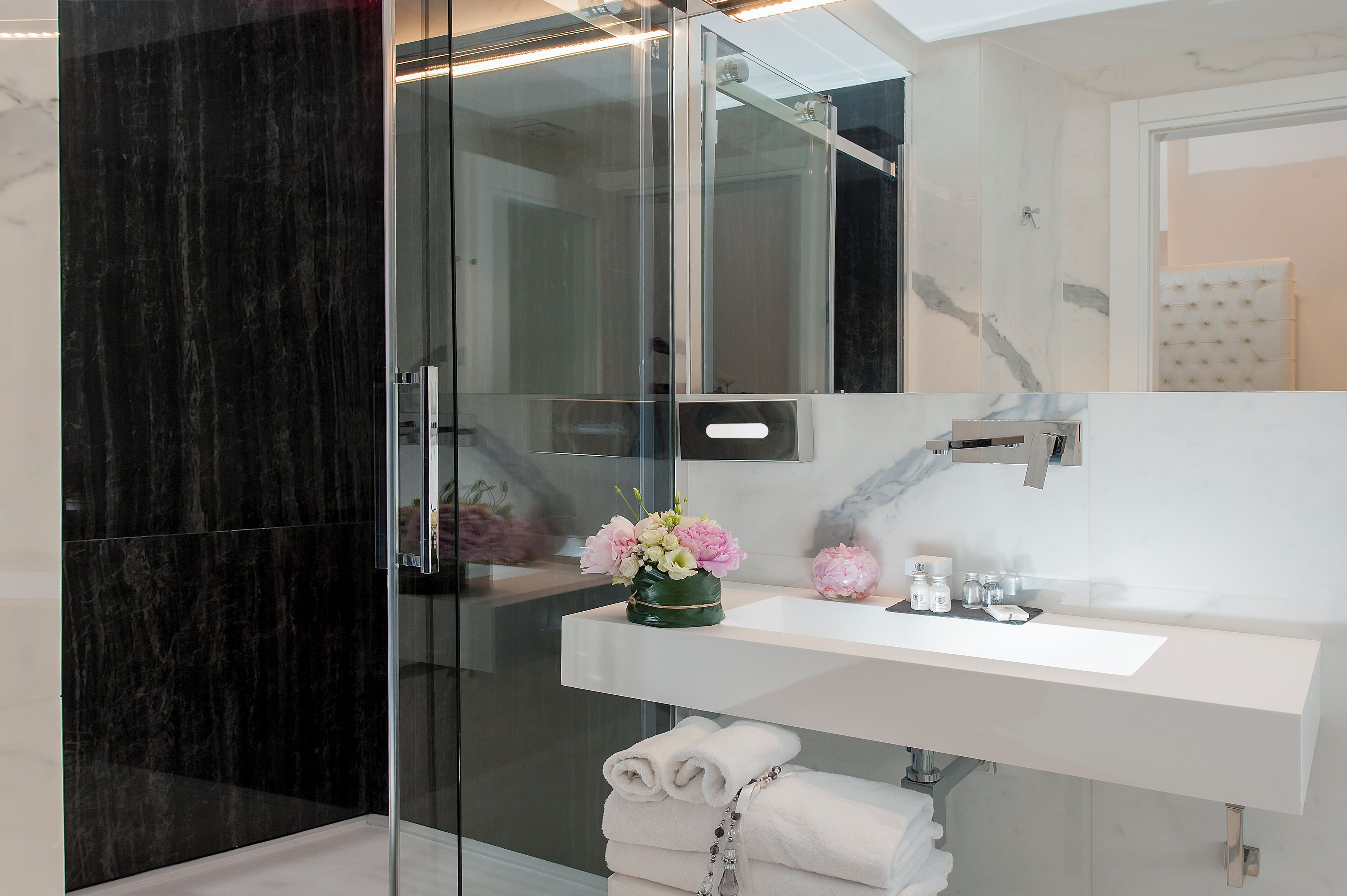 A modern bathroom with a glass shower enclosure, a white vanity with a mirror, and a vase of flowers.
