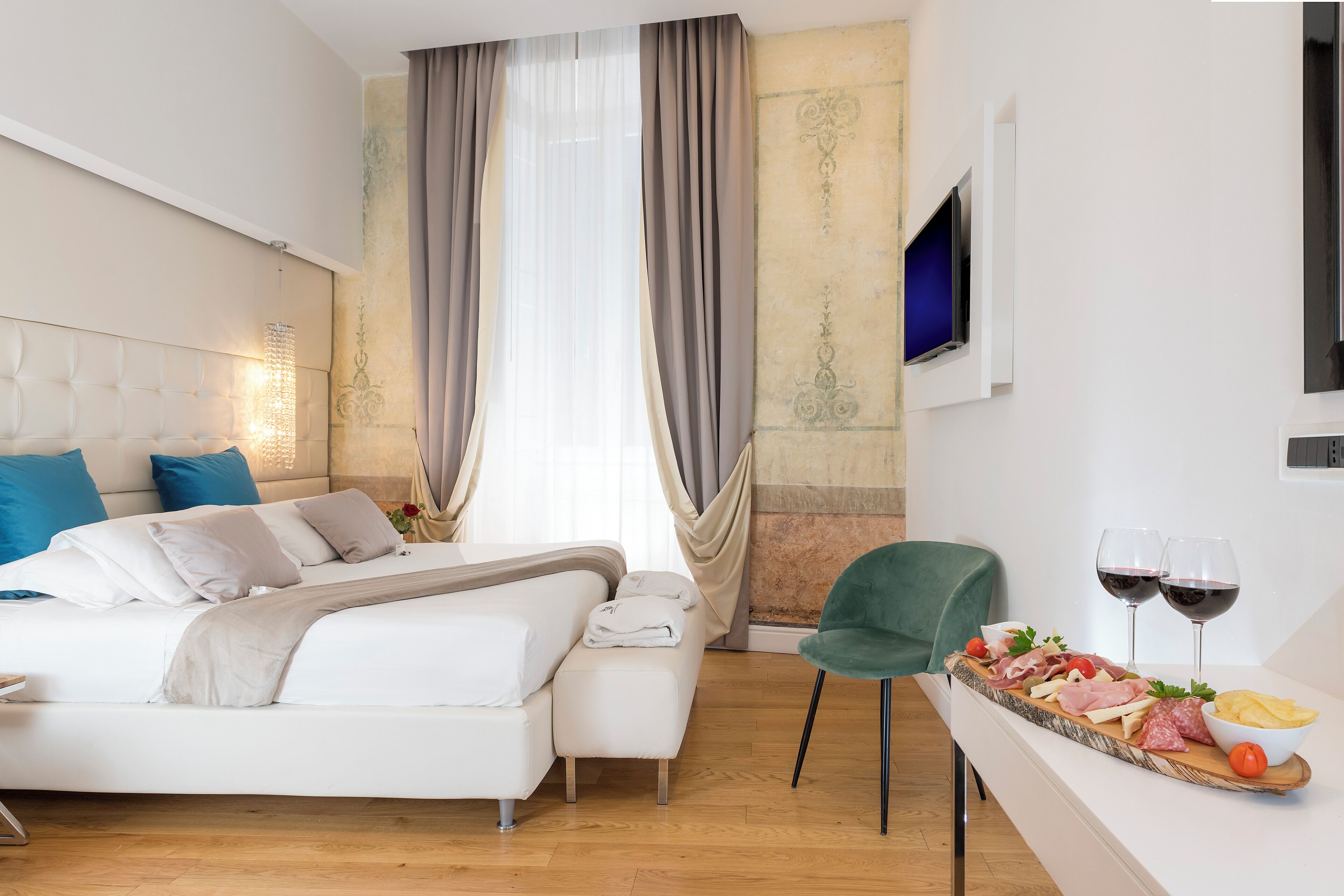 A modern hotel room with a bed, a breakfast bar with a charcuterie board, and a television mounted on the wall.
