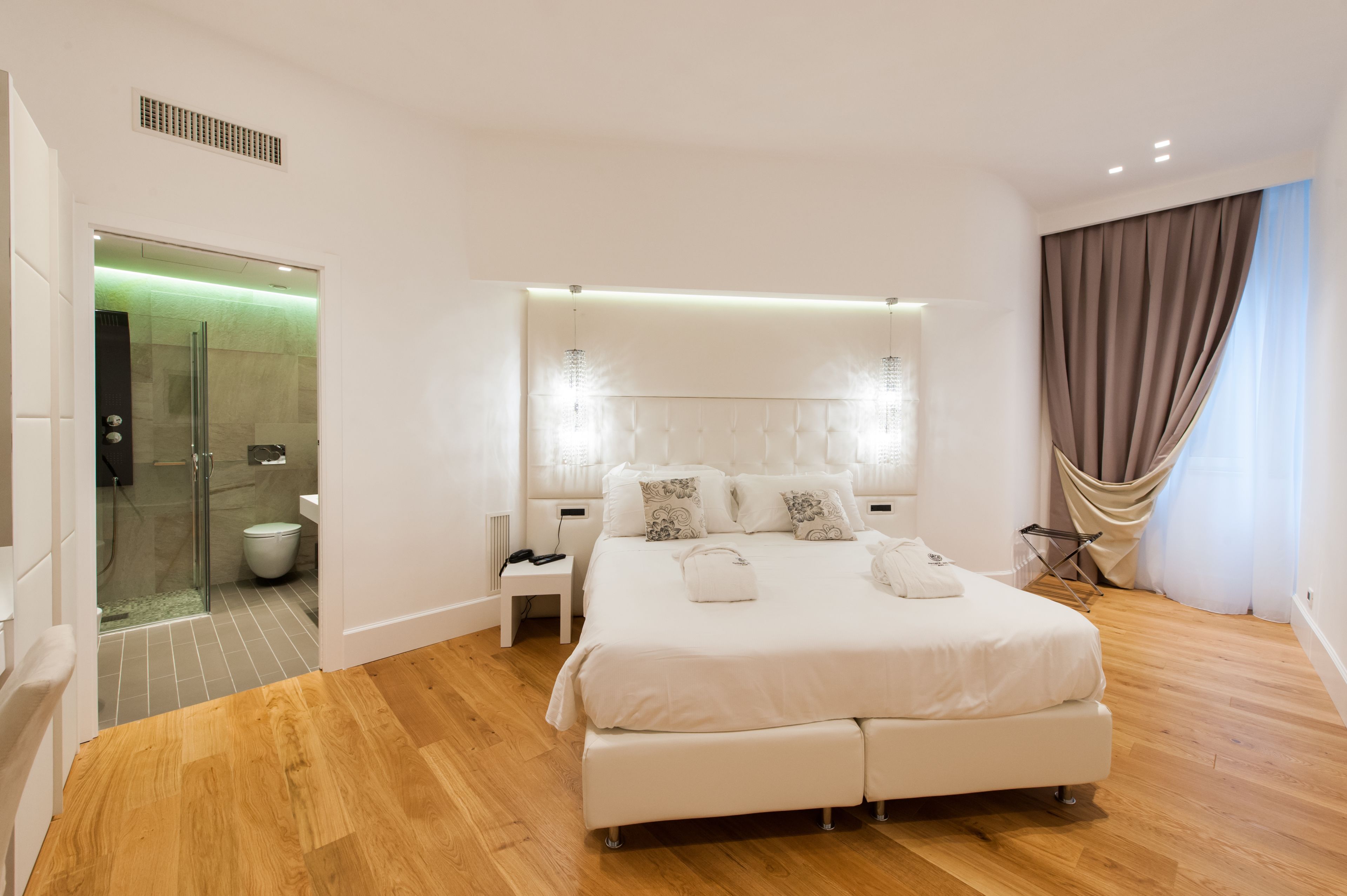 Un dormitorio moderno con una cama grande, mesitas de noche, cabina de ducha de vidrio y vistas al exterior.