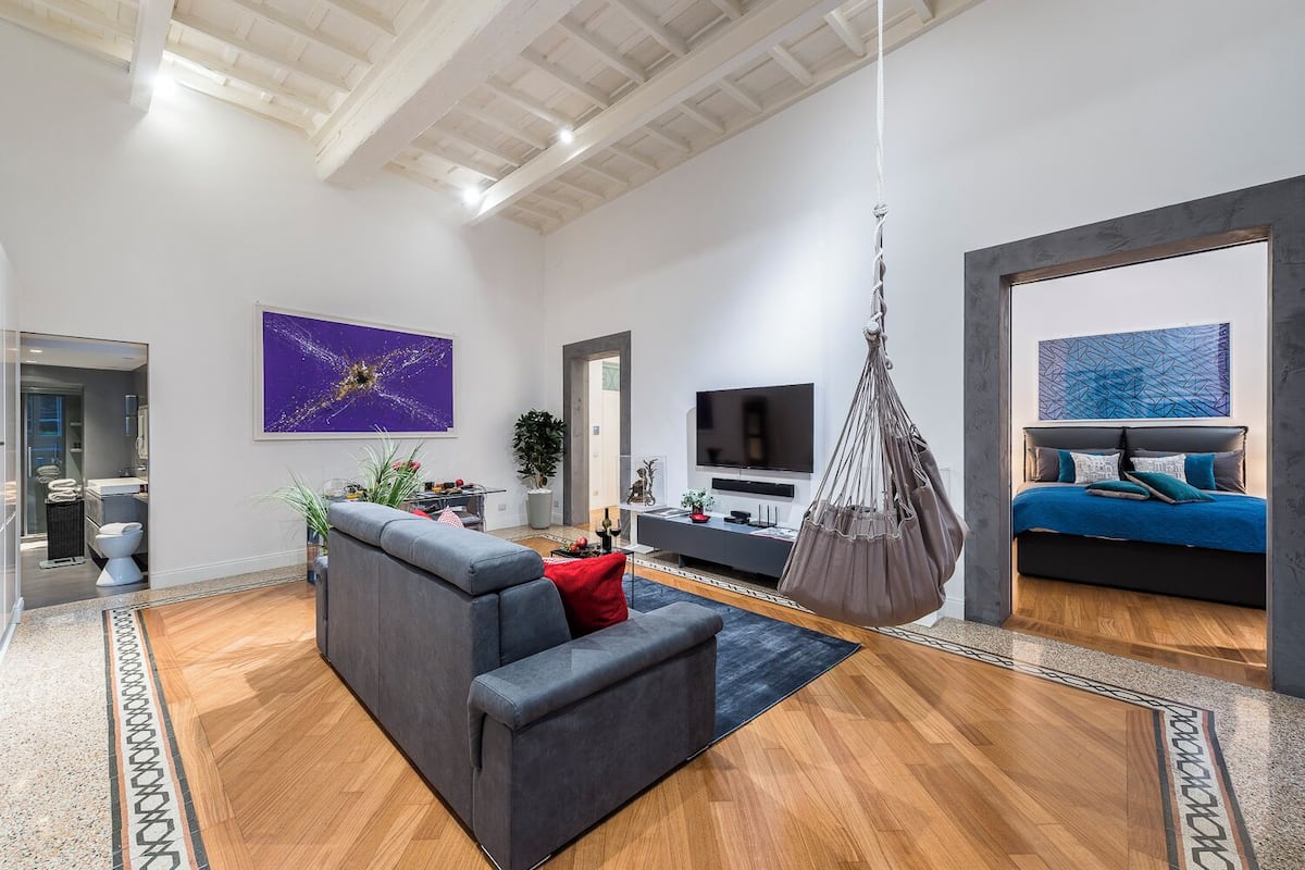 A modern living room with a grey sofa, a hanging chair, a TV, and artwork on the walls.