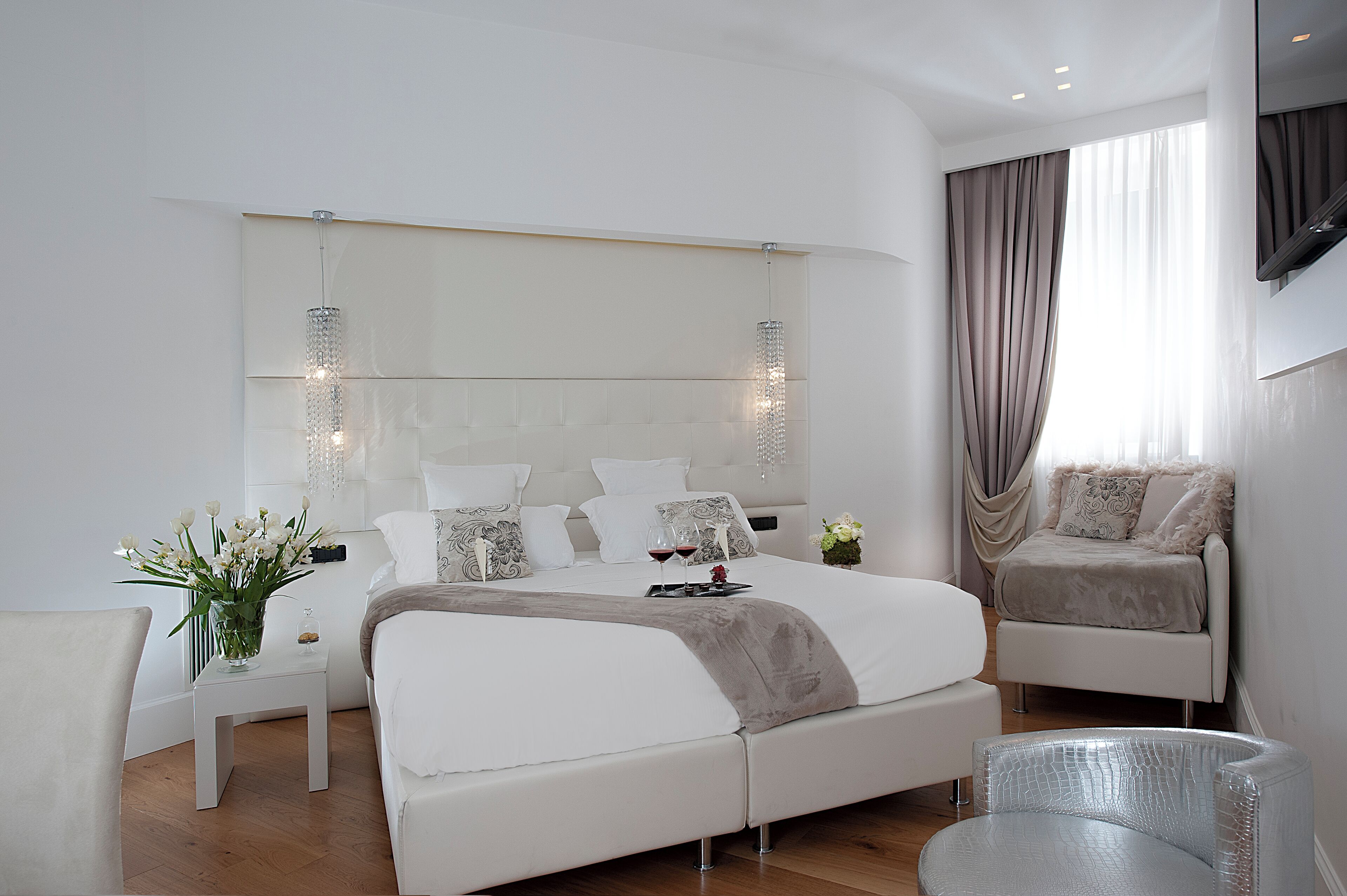 A modern bedroom with a large bed, bedside tables, a seating area, and a TV mounted on the wall.