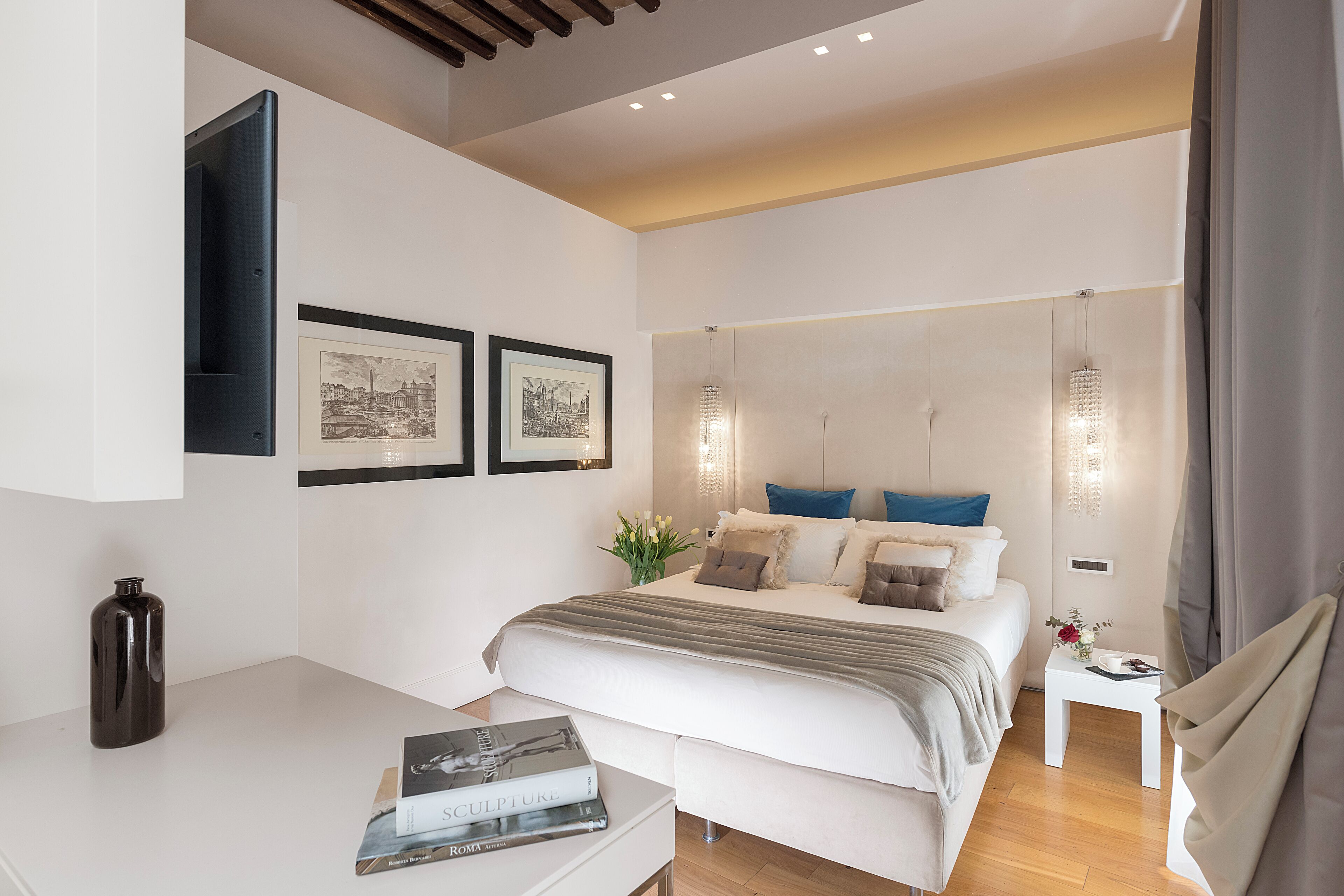 A modern bedroom with a large bed, bedside tables, framed pictures, and a small table with a vase.