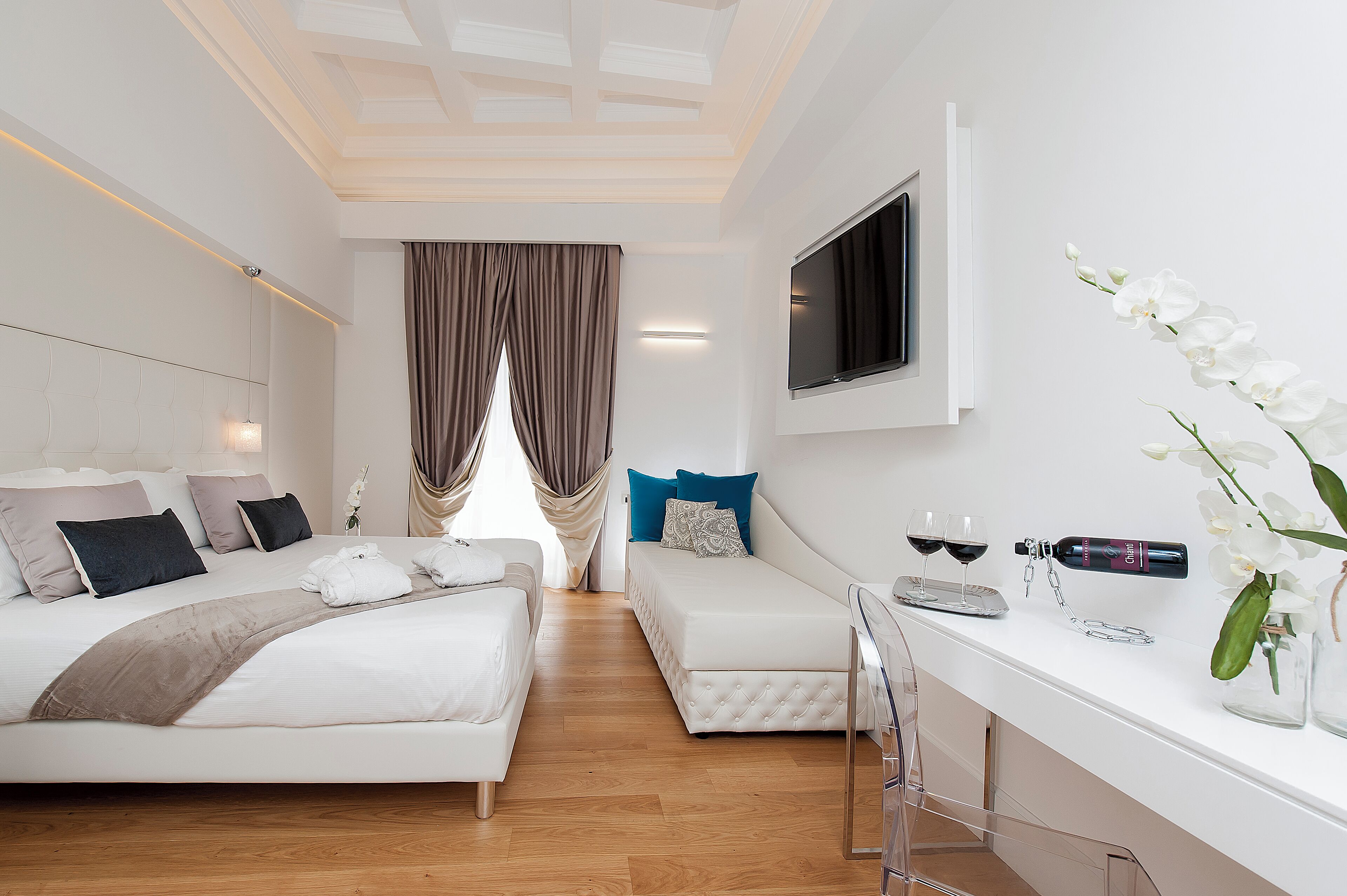 Une chambre d’hôtel moderne avec un grand lit, un petit canapé, une télévision et un minibar.