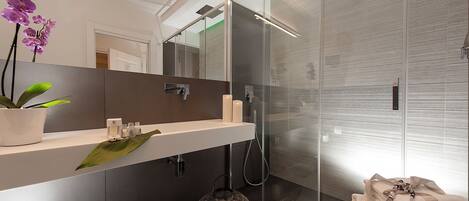 Un baño moderno con cabina de ducha de vidrio, tocador blanco con espejo y una orquídea en maceta.