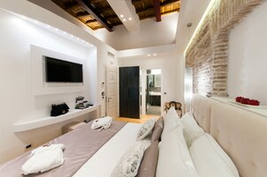 A modern bedroom with a large bed, a TV mounted on the wall, a vanity with a mirror, and a brick accent wall.