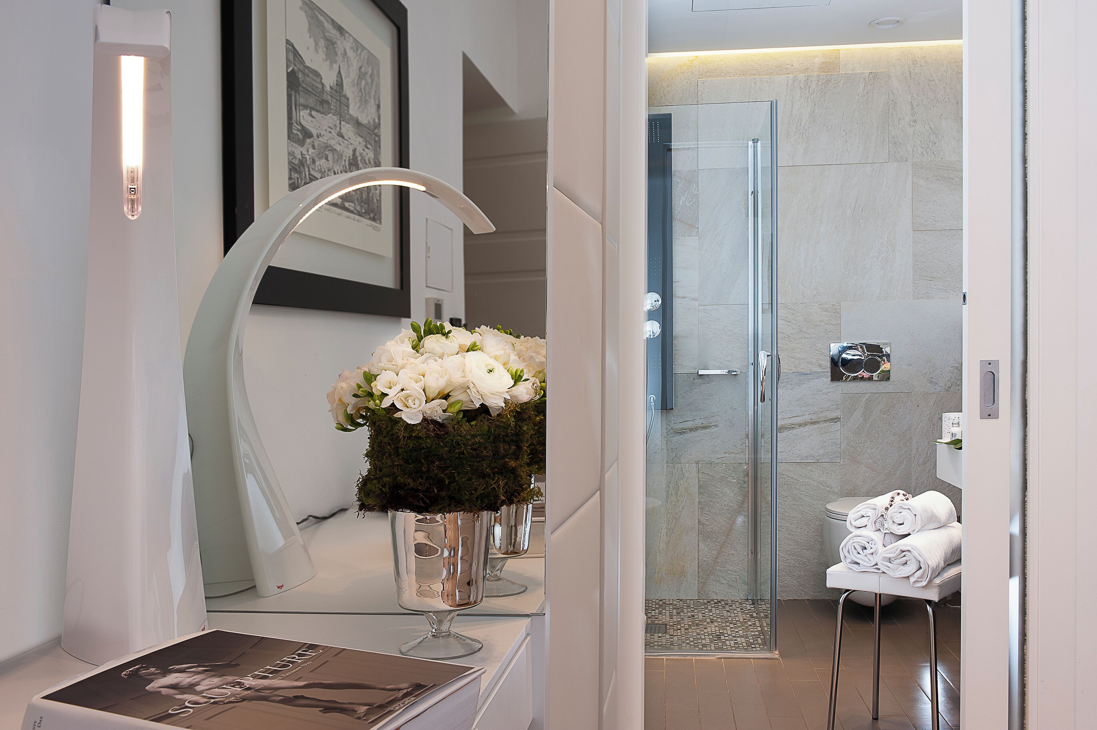 A modern bathroom with a glass shower, a white sink with a vase of flowers, and neatly folded towels.