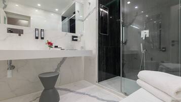 Un baño moderno con tocador de mármol, cabina de ducha de cristal y una toalla blanca sobre un banco.