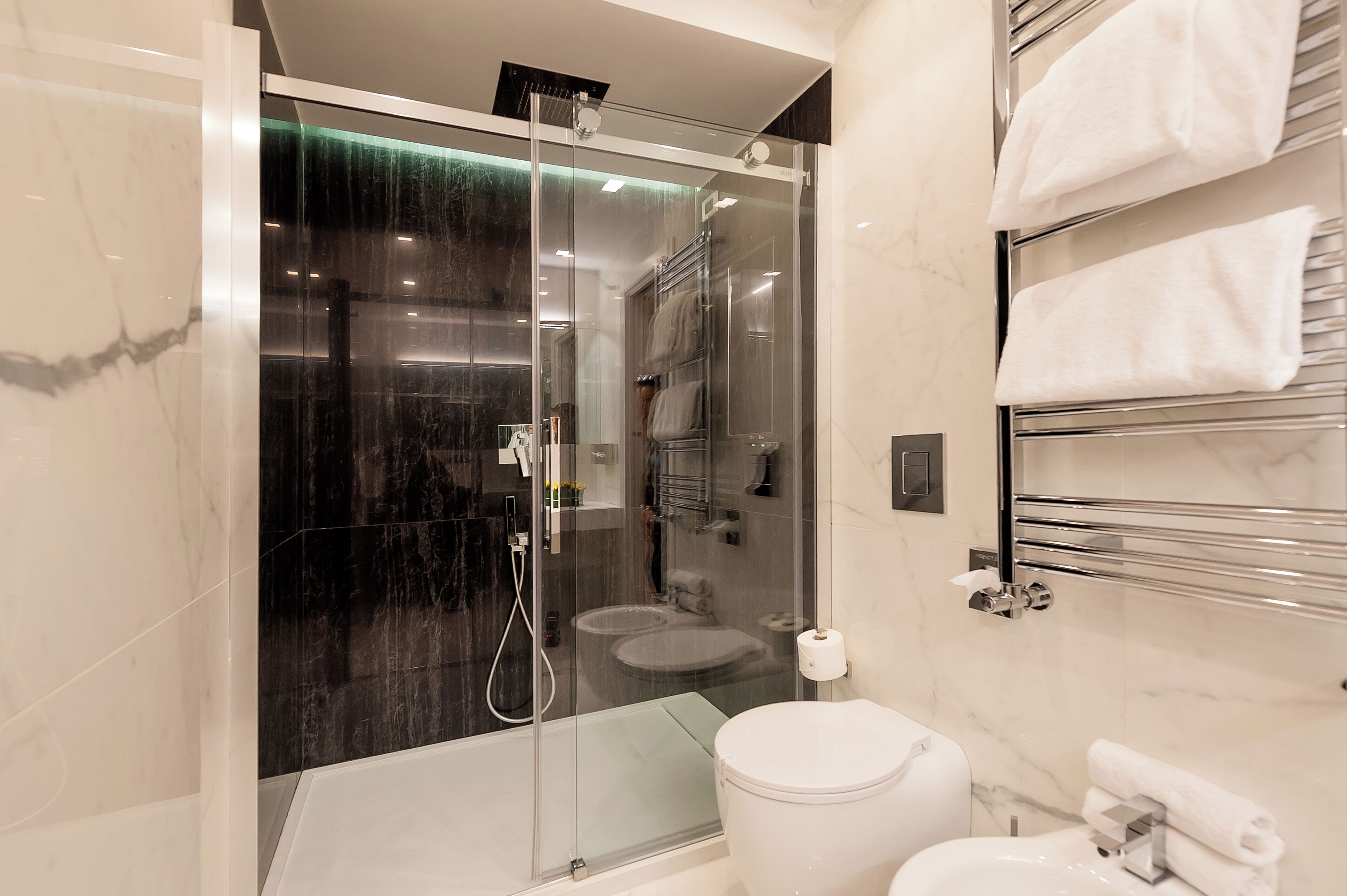 A modern bathroom with a glass-enclosed shower, a white toilet, and a marble-tiled wall.