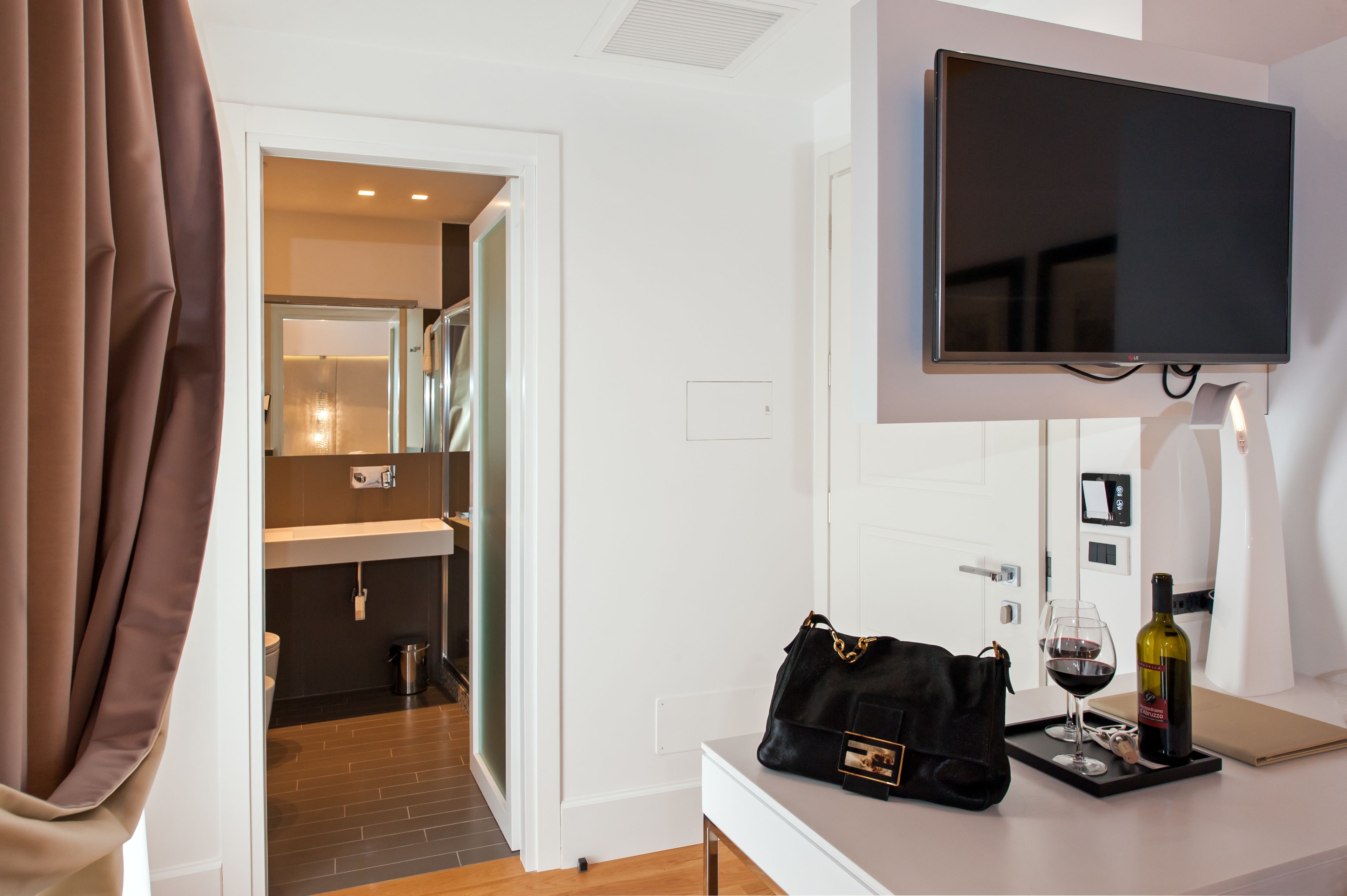 Habitación de hotel con televisión, minibar, baño y ventana con cortinas.