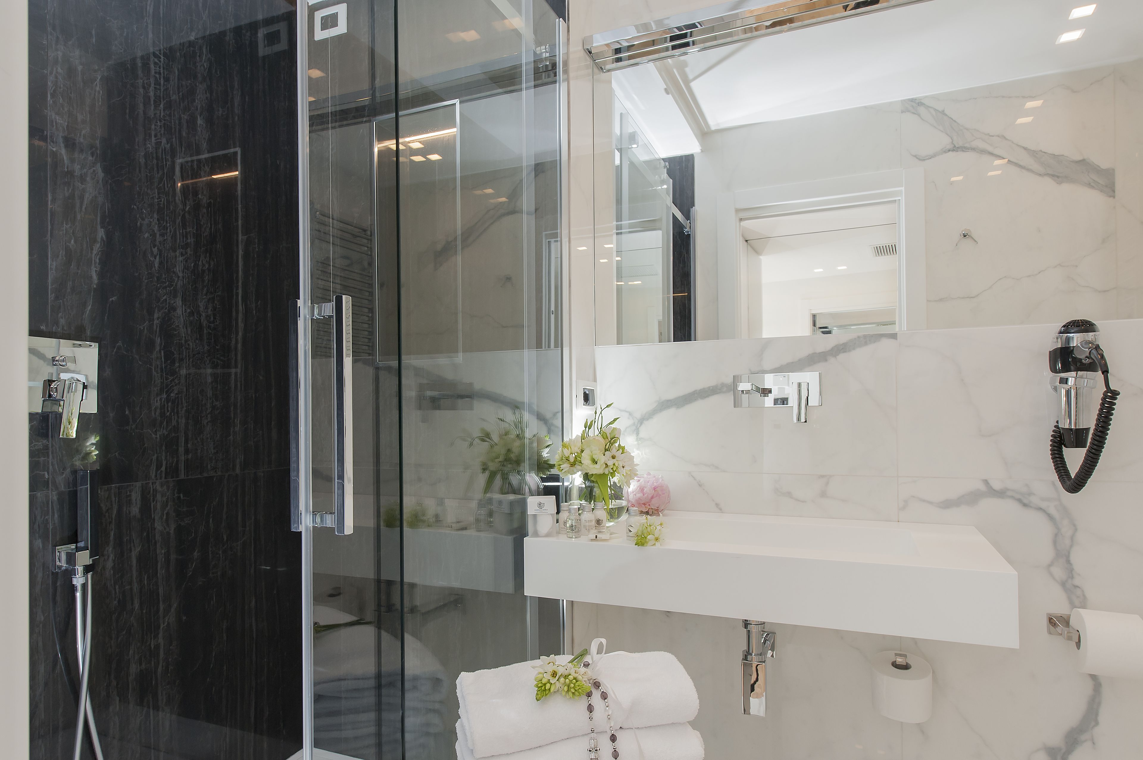 A modern bathroom with a glass shower enclosure, a marble-tiled wall, a vanity with a mirror, and a towel rack.
